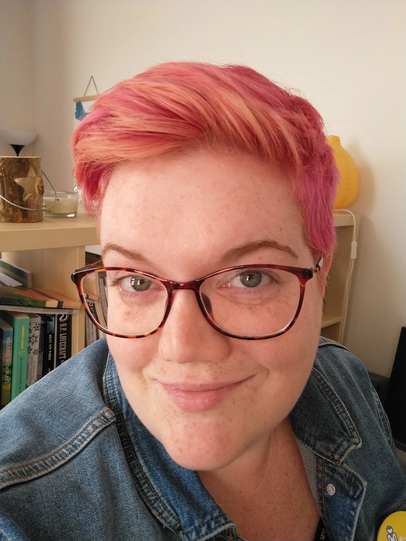 image description: photo of a white woman with glasses and short pink hair looking at the camera and smiling