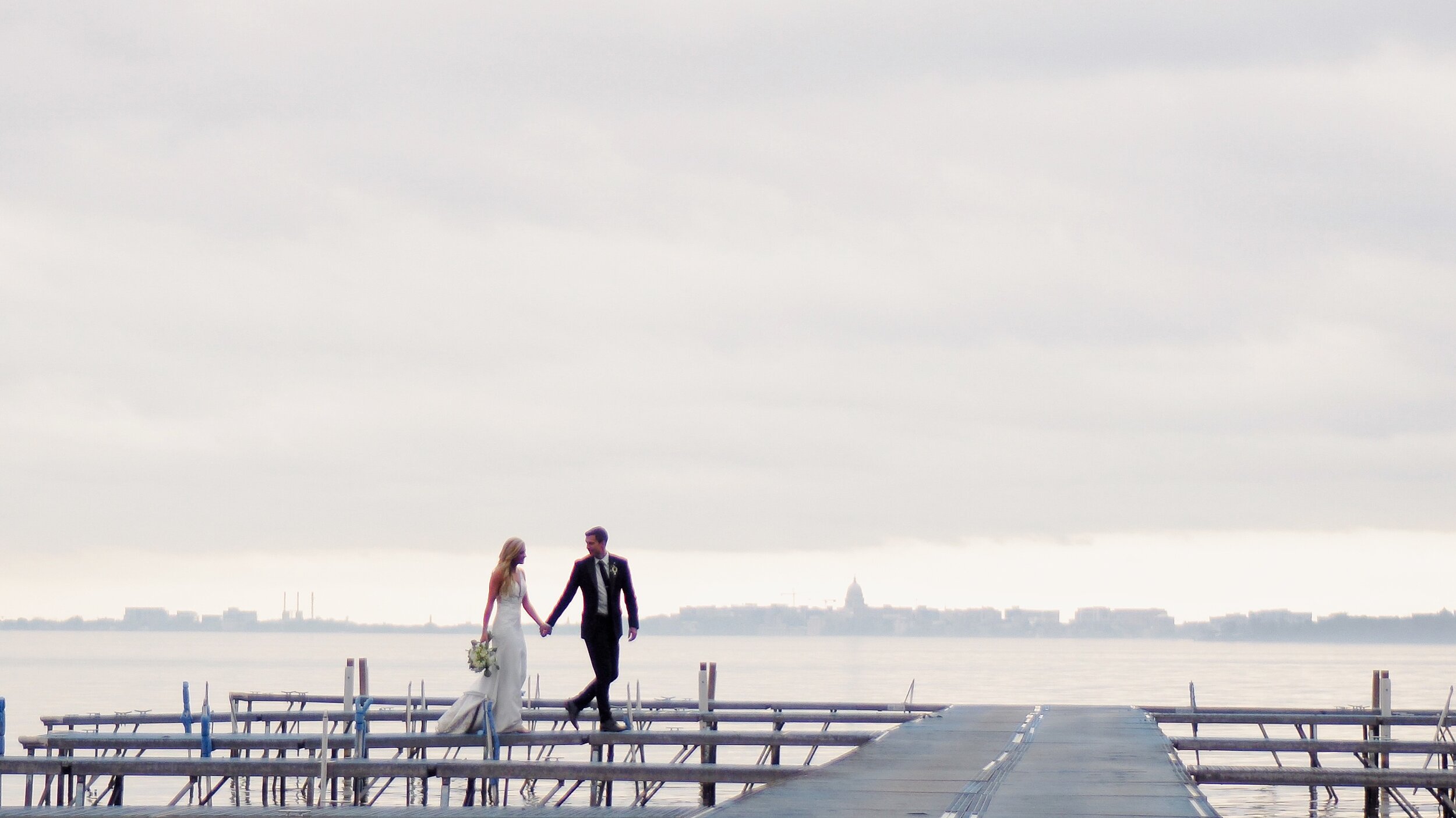 Bride and Groom walk on the dock at Bishops Bay Country Club overlooking the capitol in Madison WI