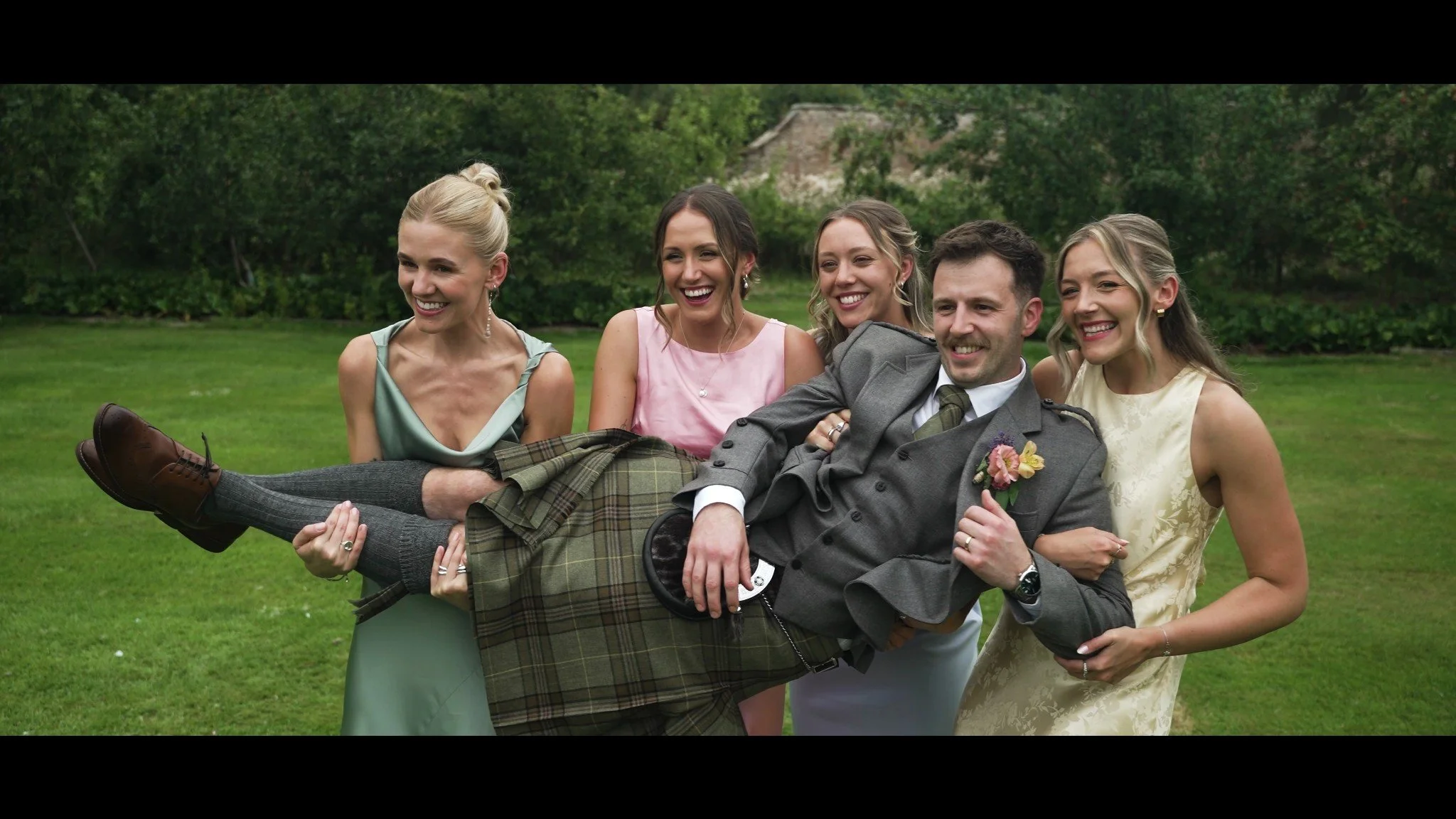 Rhys being lifted by members of the wedding party on the lawn