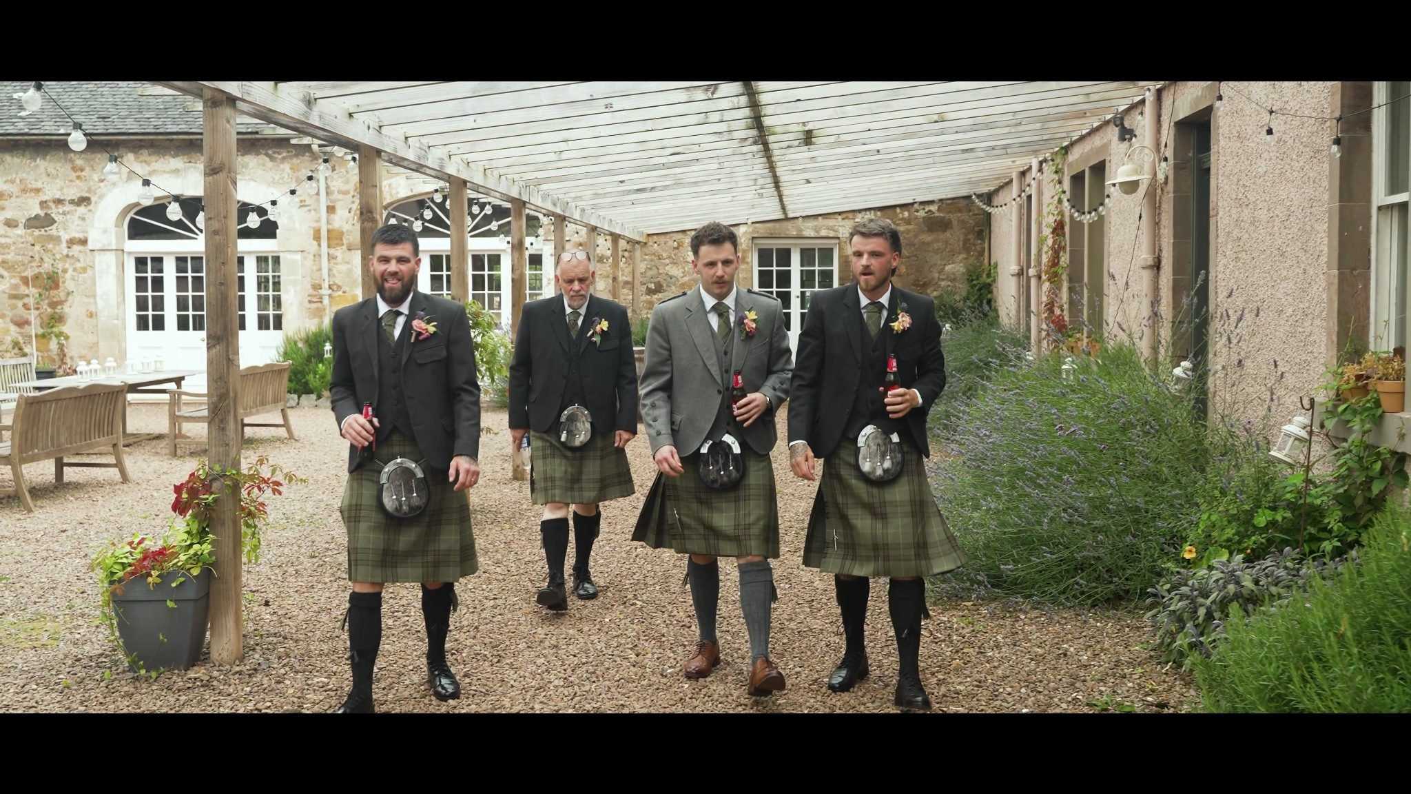 Rhys and three groomsmen walking beside a stone building