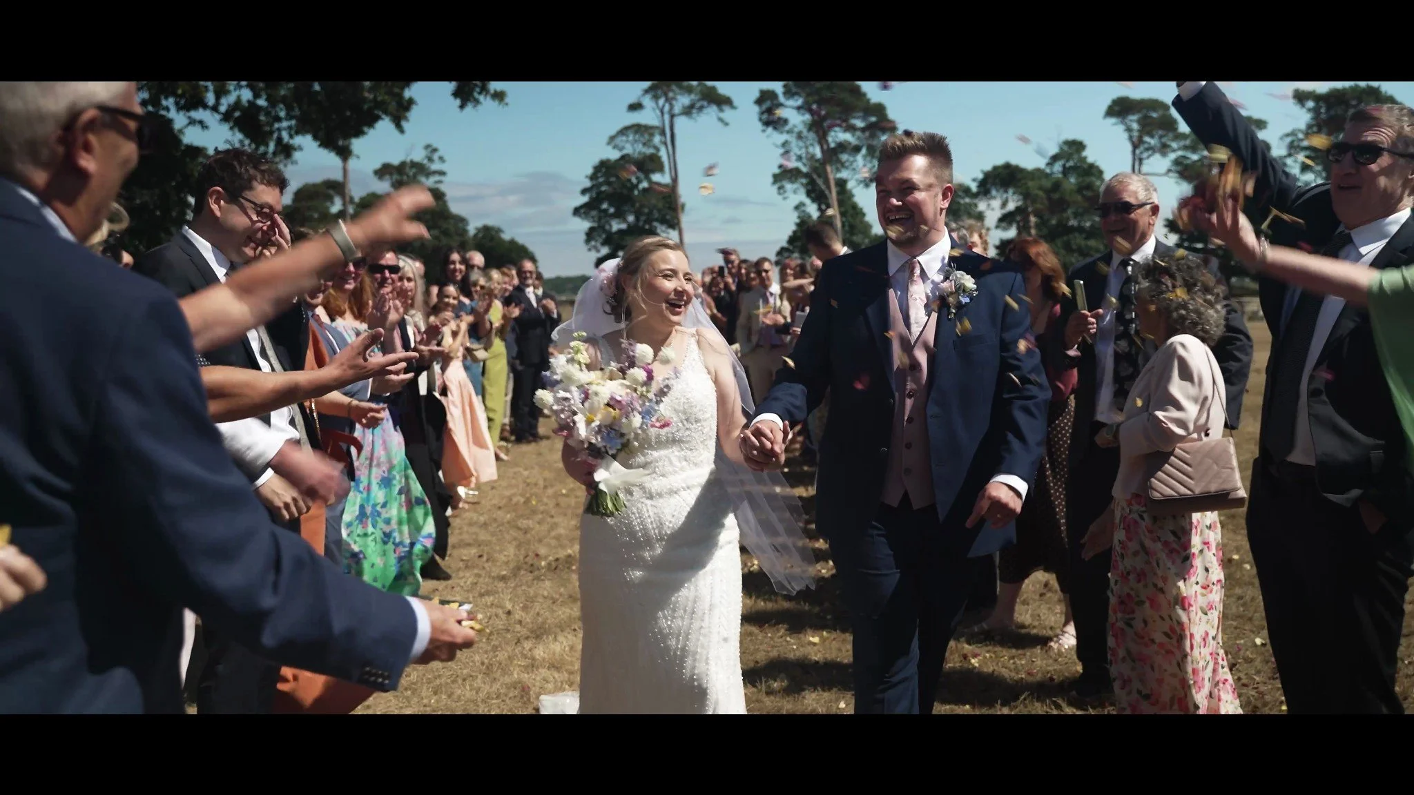 Hannah and David smiling as guests celebrate around them outdoors