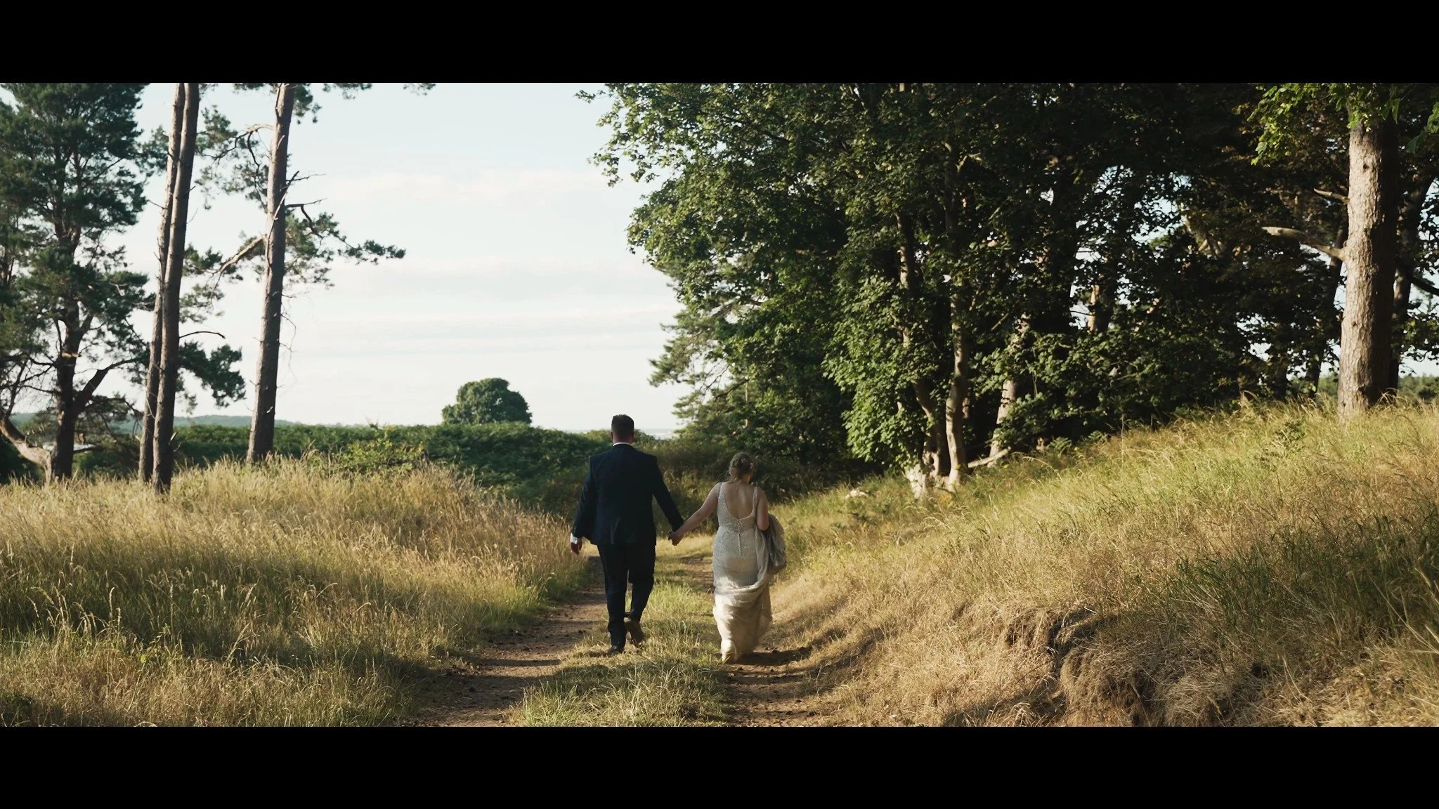 Hannah and David walking hand in hand along a sunlit woodland path