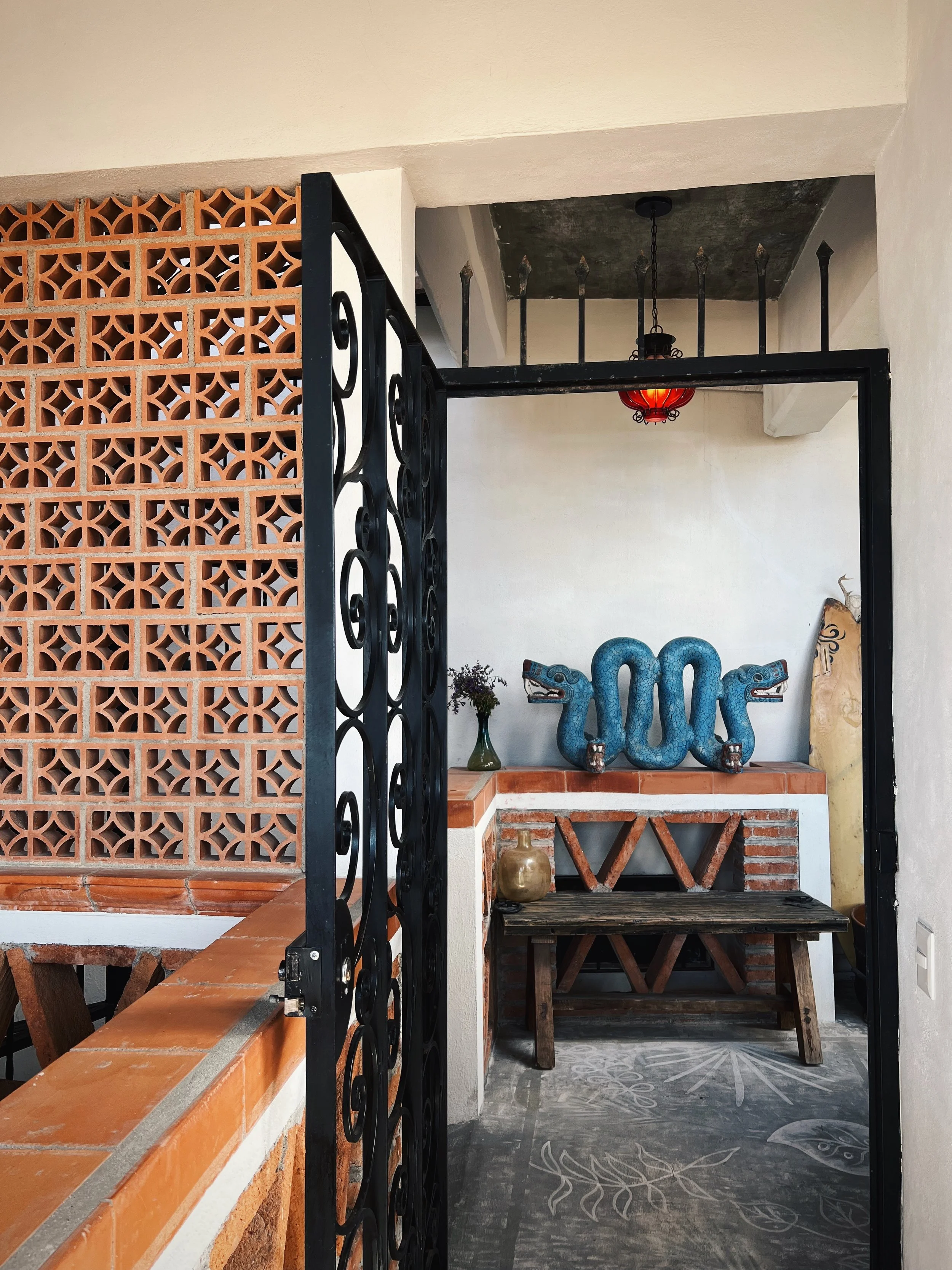 Decorative outdoor area with a brick wall, black wrought iron gate, rustic wooden bench, and a blue dragon sculpture with the number 2006, a vase with flowers, and a gold decorative item on a brick ledge.