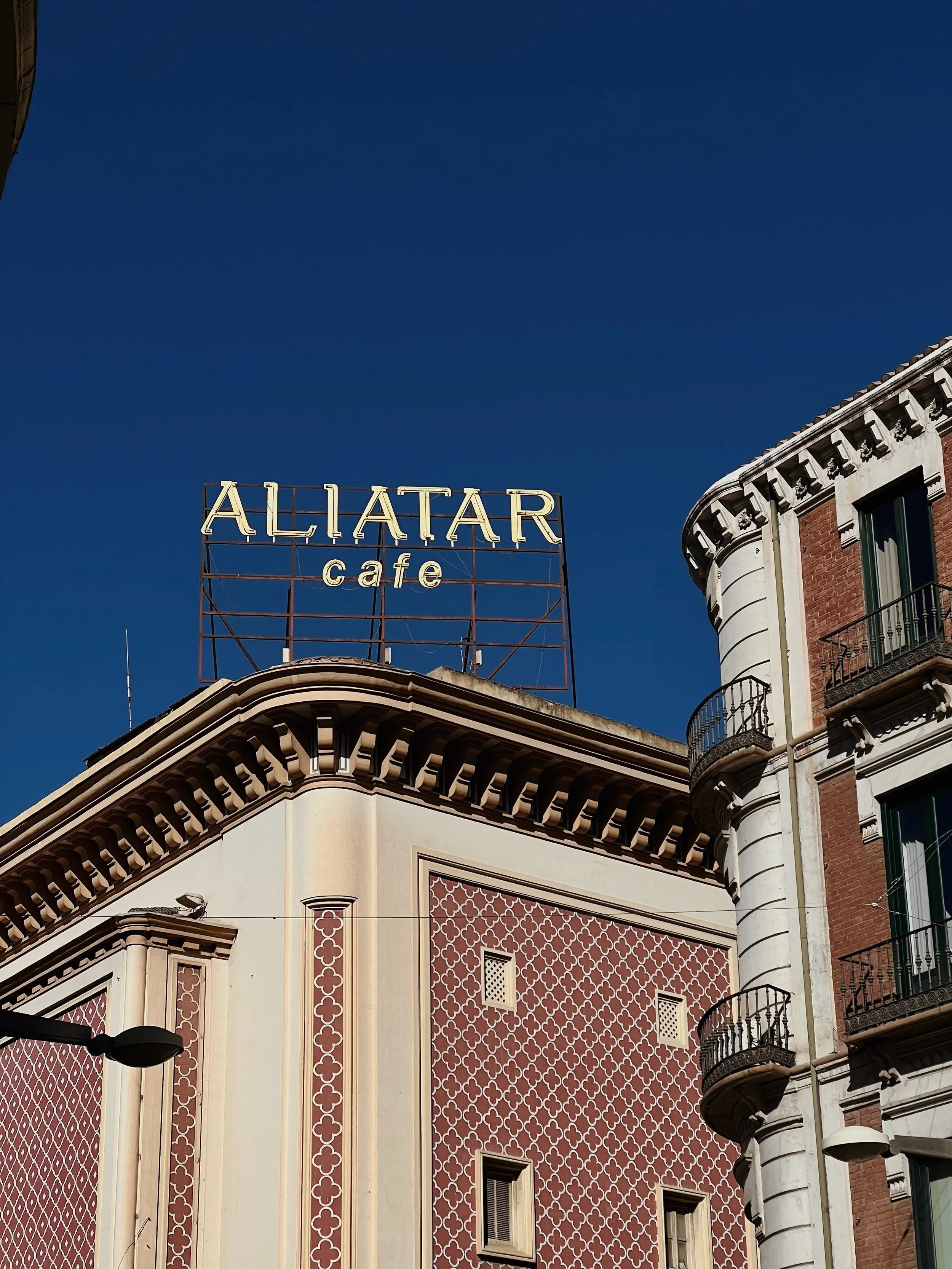 A sign reading 'ALIATAR cafe' atop a building with ornate architectural details, against a dark blue sky.