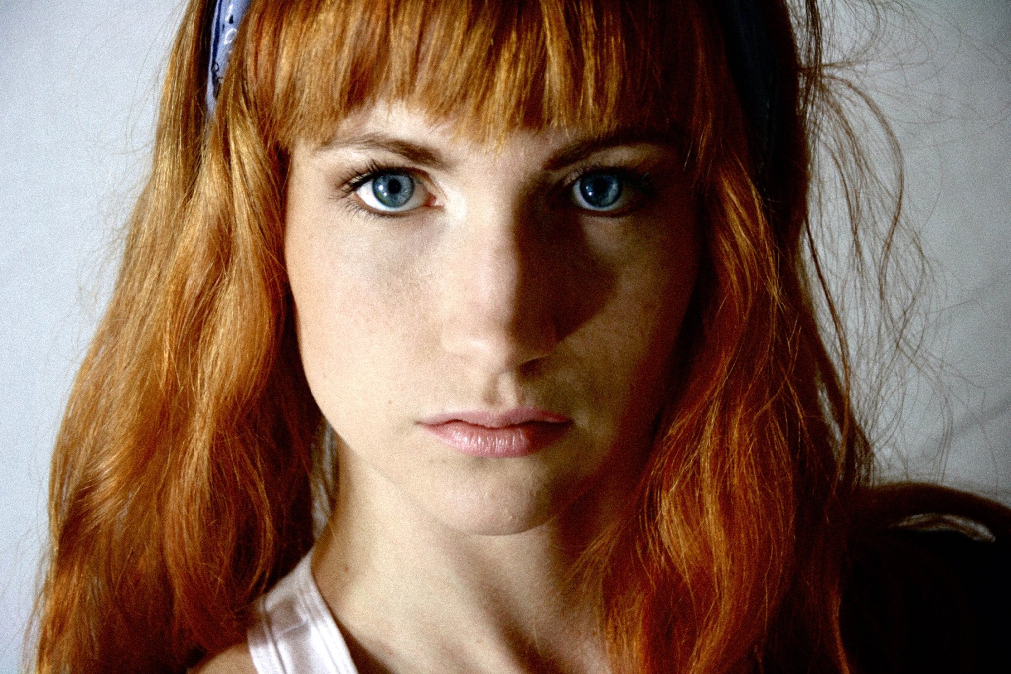 A close-up of a young woman with red hair, blue eyes, and freckles. She has a headband and is looking directly at the camera.