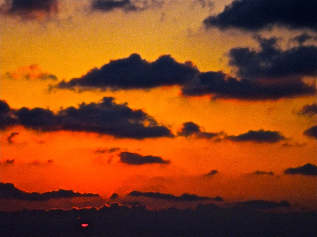 Sun setting with an orange and yellow sky and dark clouds.