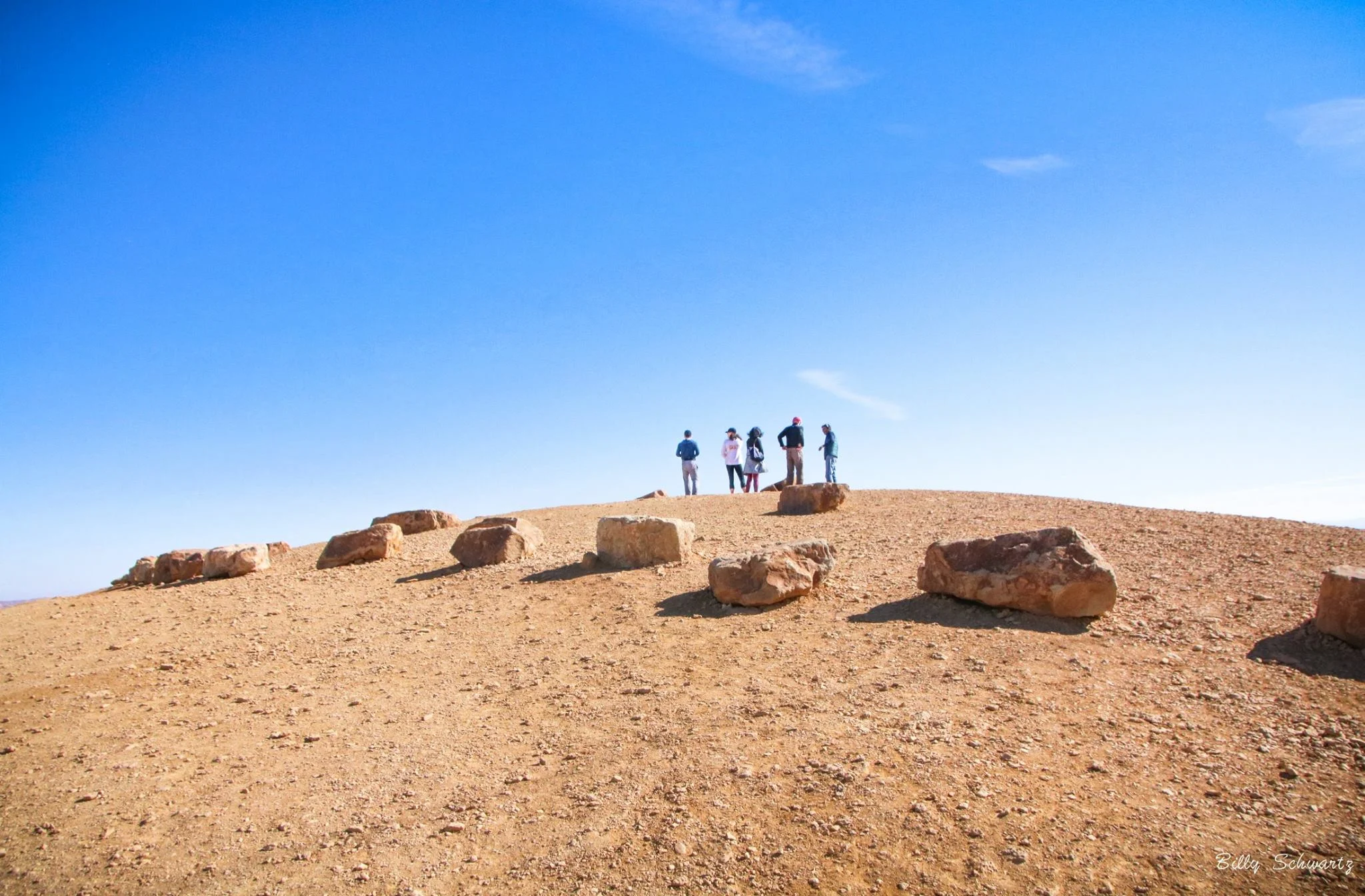 Group of five people standing on a hilltop with large rocks, under a clear blue sky.