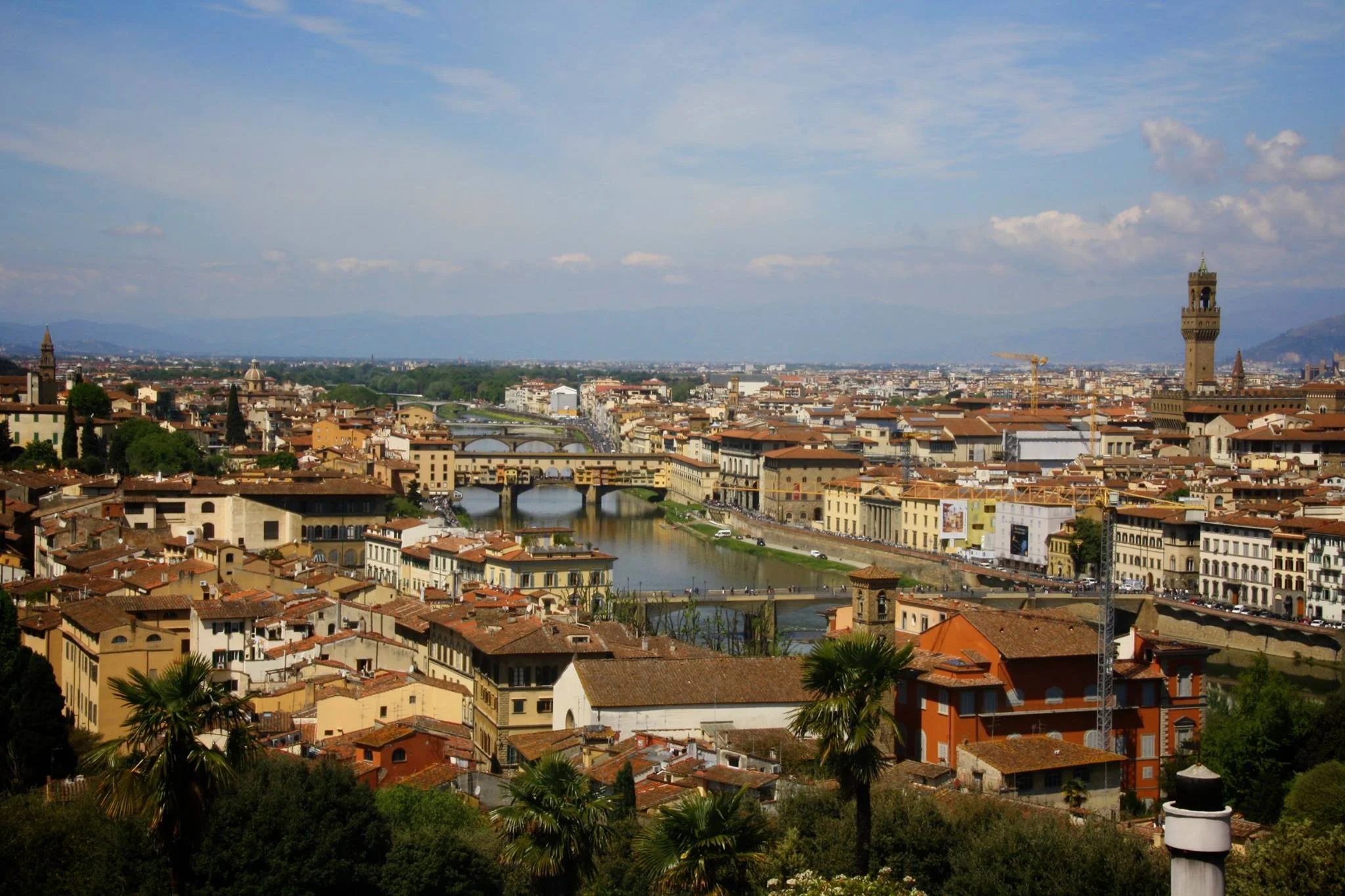 Panoramic view of Florence, Italy, with the Arno River, historic buildings, multiple bridges, and a blue sky with clouds.