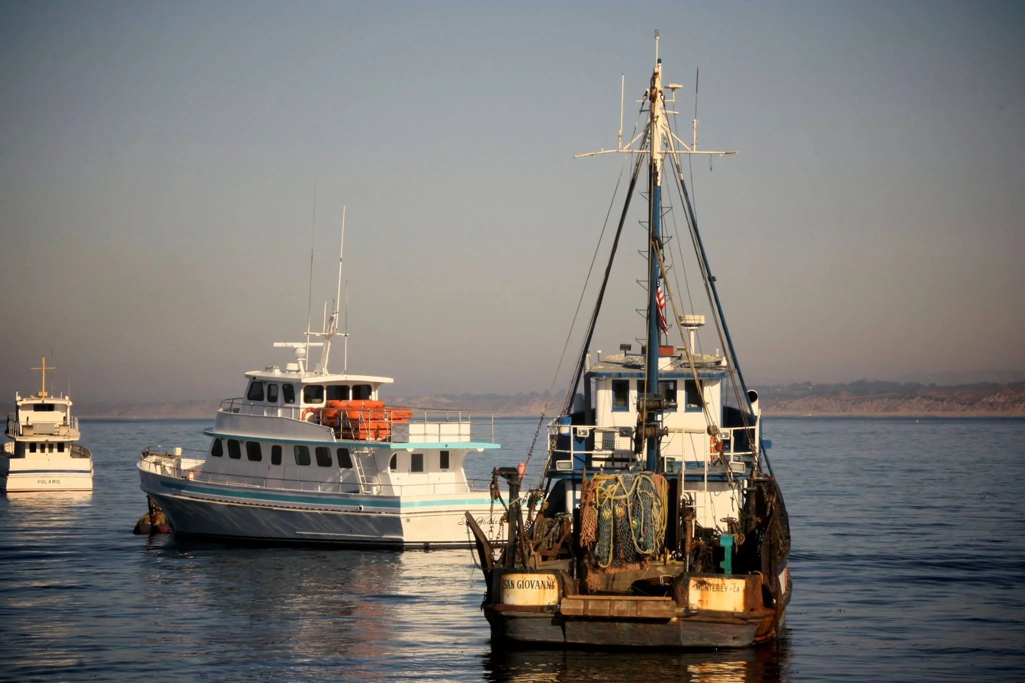 Three boats floating on calm water with a distant shoreline.