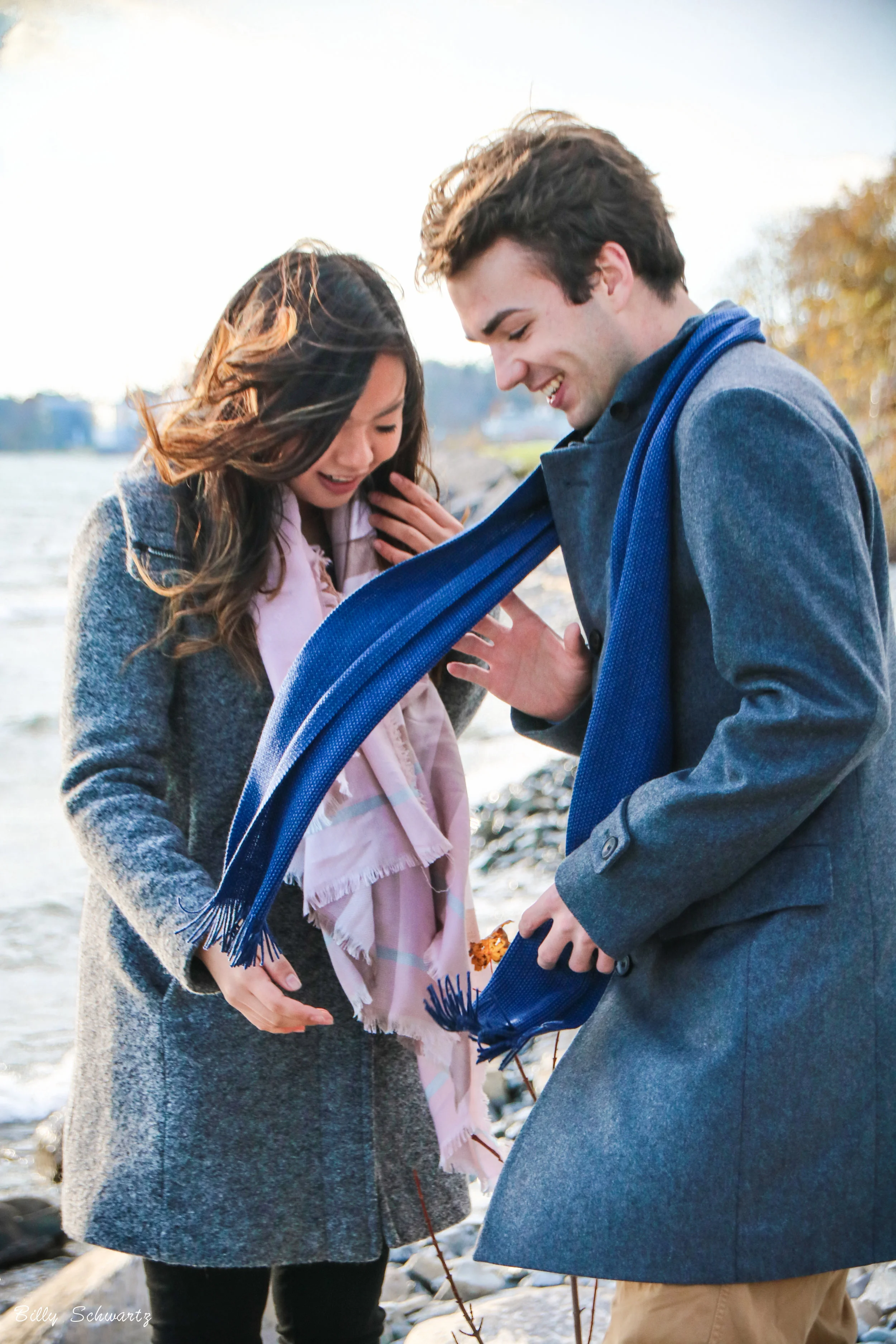 A young couple standing by a river, exchanging scarves as a sign of affection.