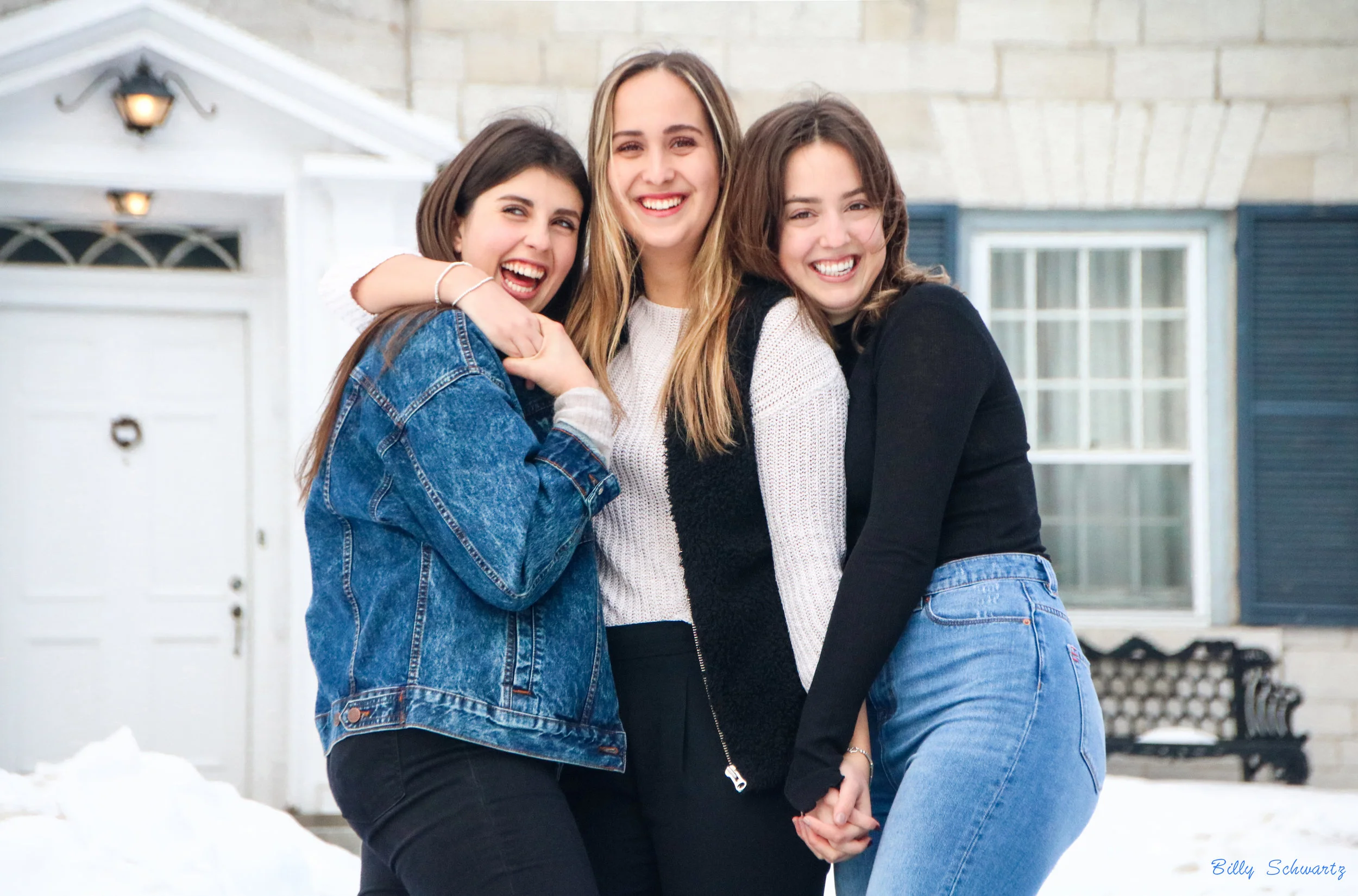 Four young women smiling and hugging outside a house in winter.