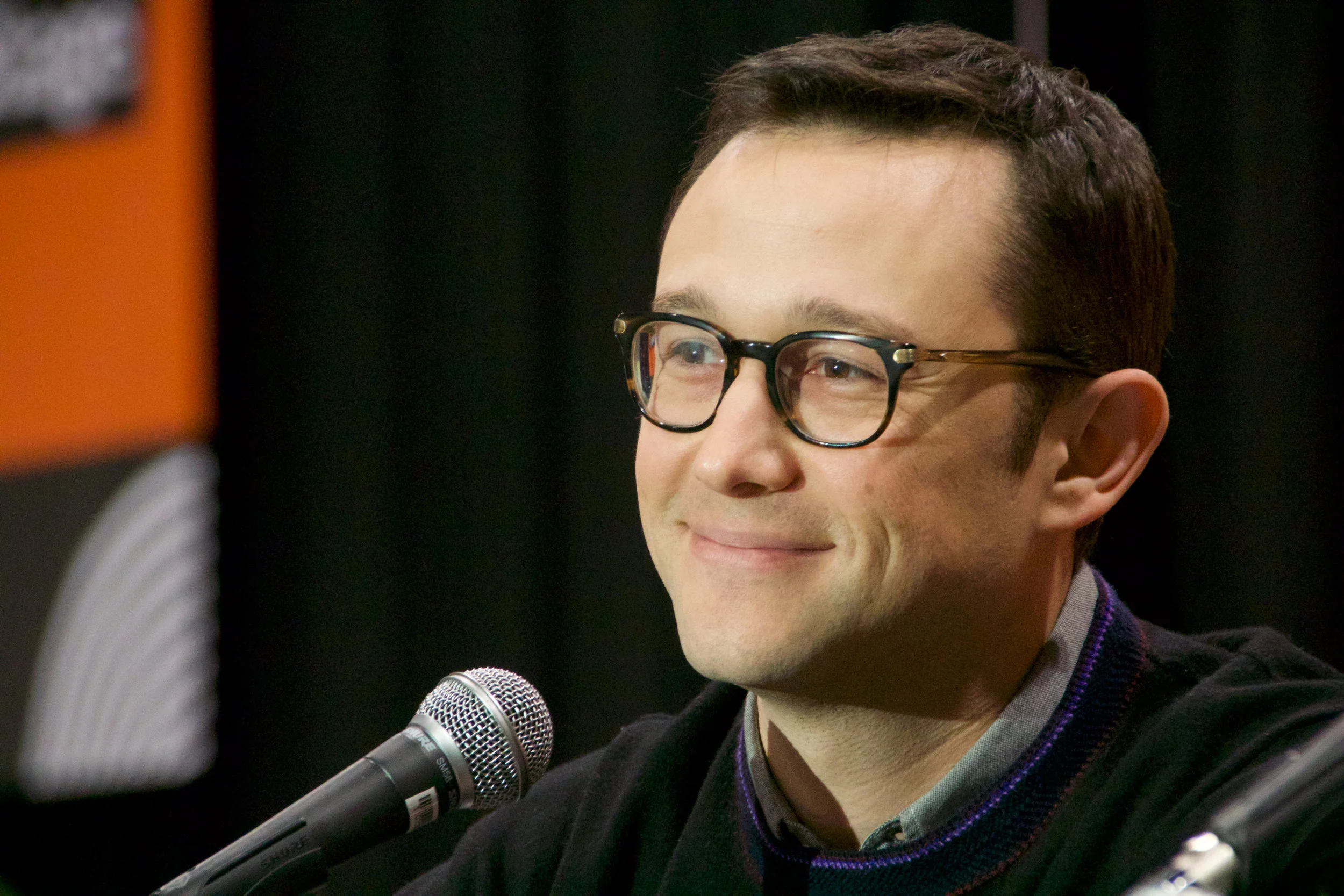 A man with glasses smiling, sitting in front of a microphone at a panel or interview.