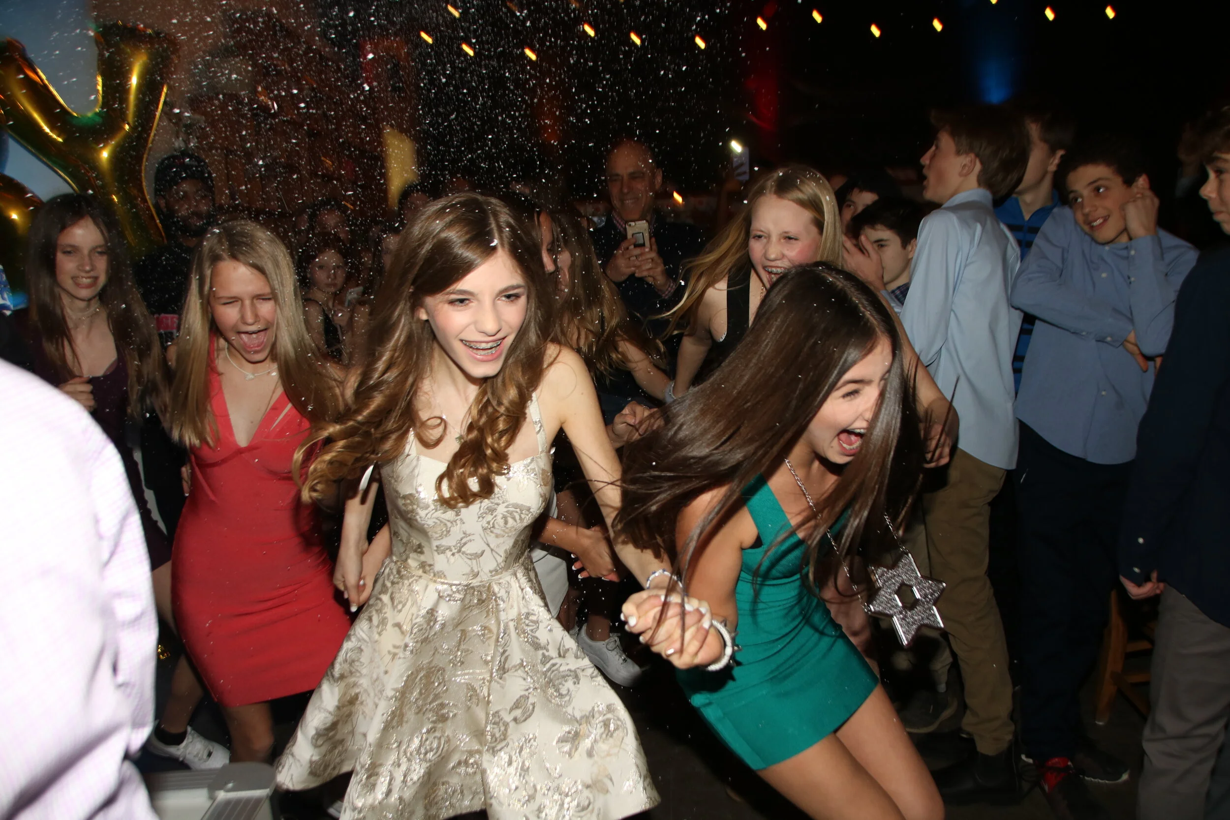 Group of young girls and boys dancing and celebrating at a party or celebration, with confetti in the air and smiles on their faces.