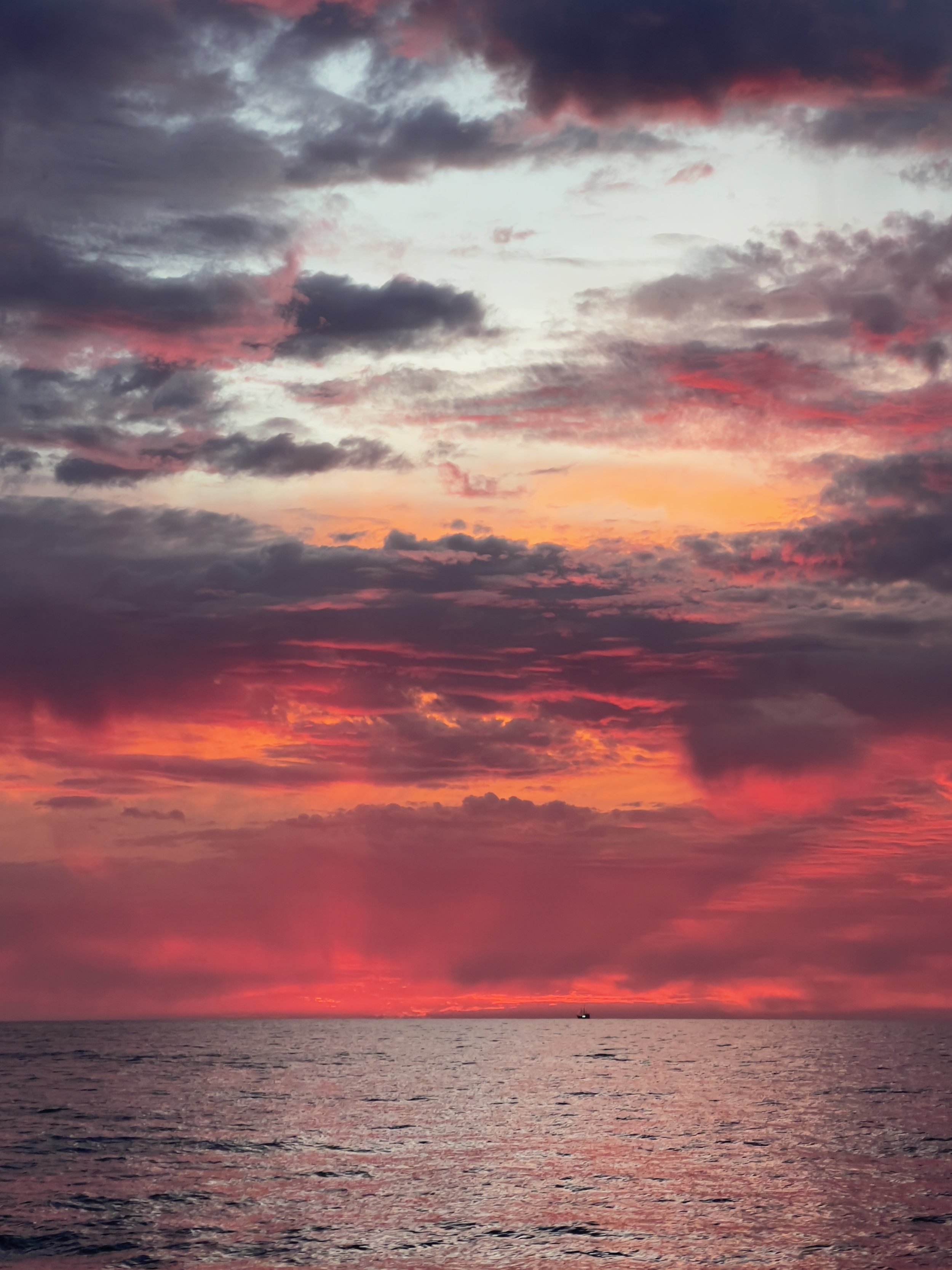 Sunset over the ocean with colorful clouds in the sky, shades of pink, purple, orange, and gray.