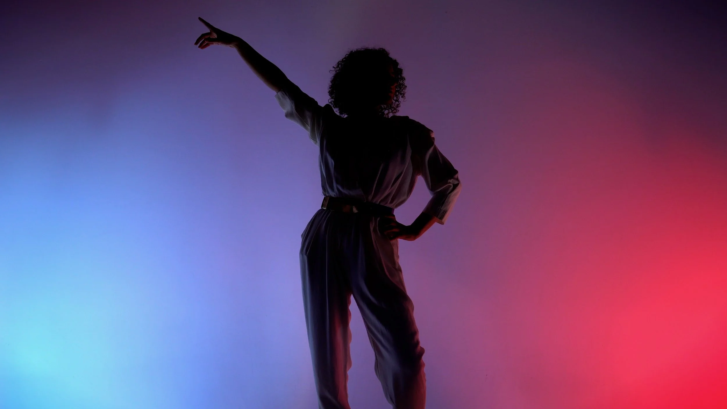 Silhouette of a woman with curly hair standing with one hand on her hip and the other extended upward, against a gradient background with pink, purple, and blue lighting.