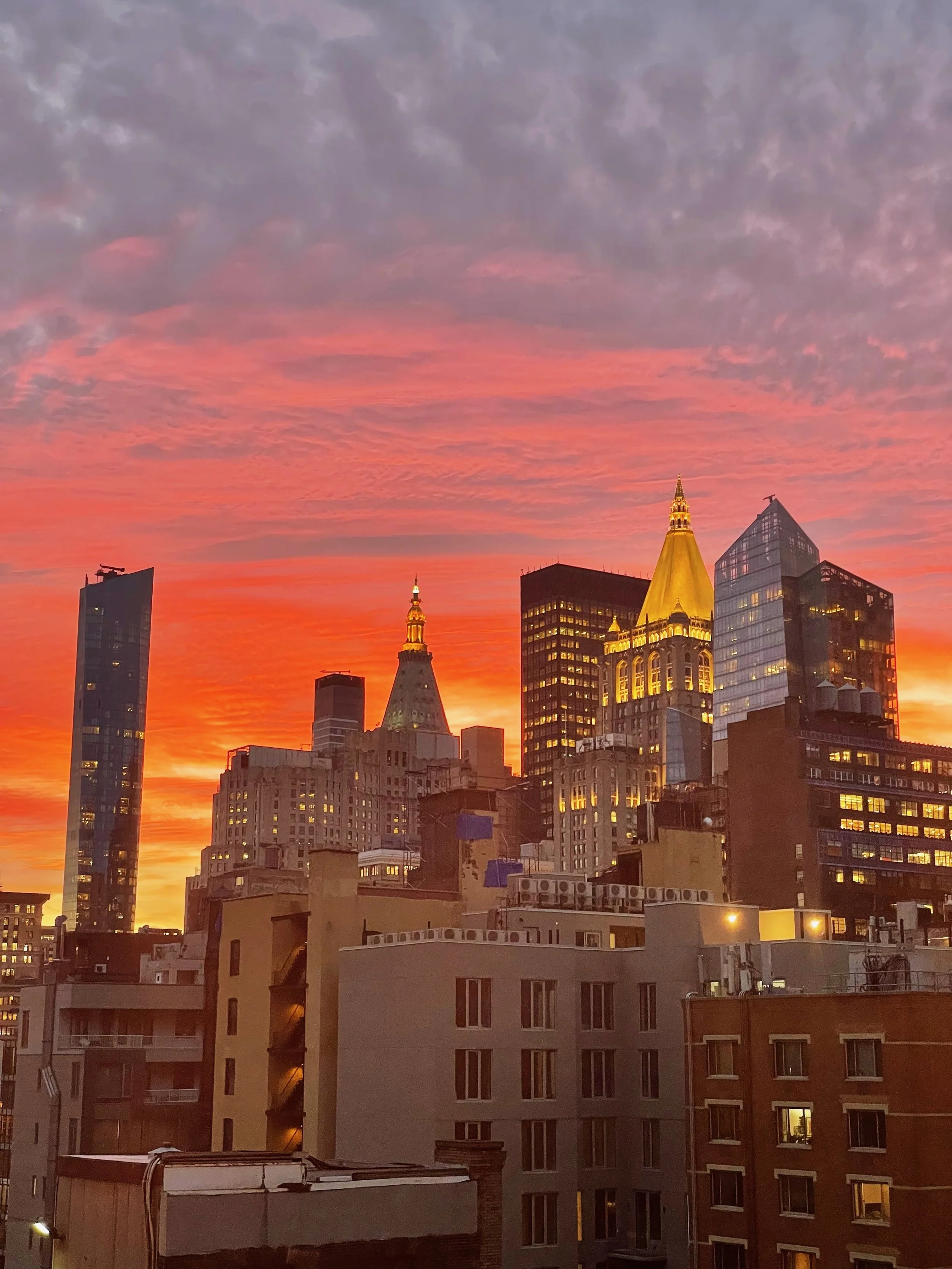 City skyline at sunset with colorful sky, including tall buildings and skyscrapers with illuminated windows.