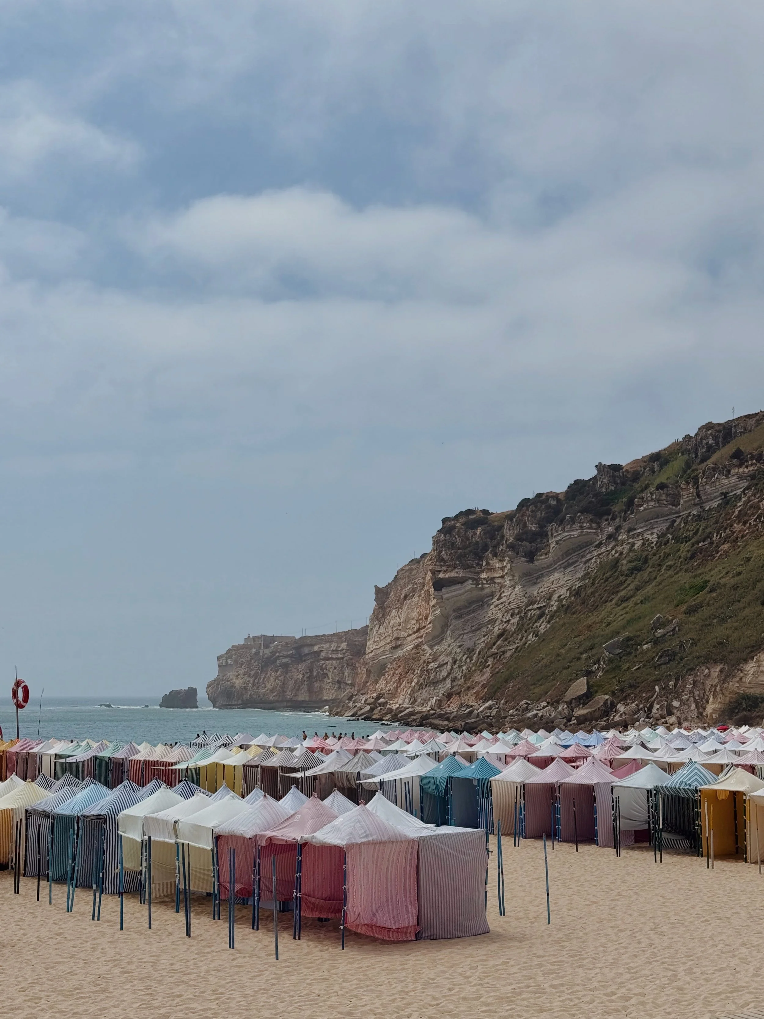 Colorful beach tents set up on Sandy Shore with cliffs in the background and cloudy sky overhead.