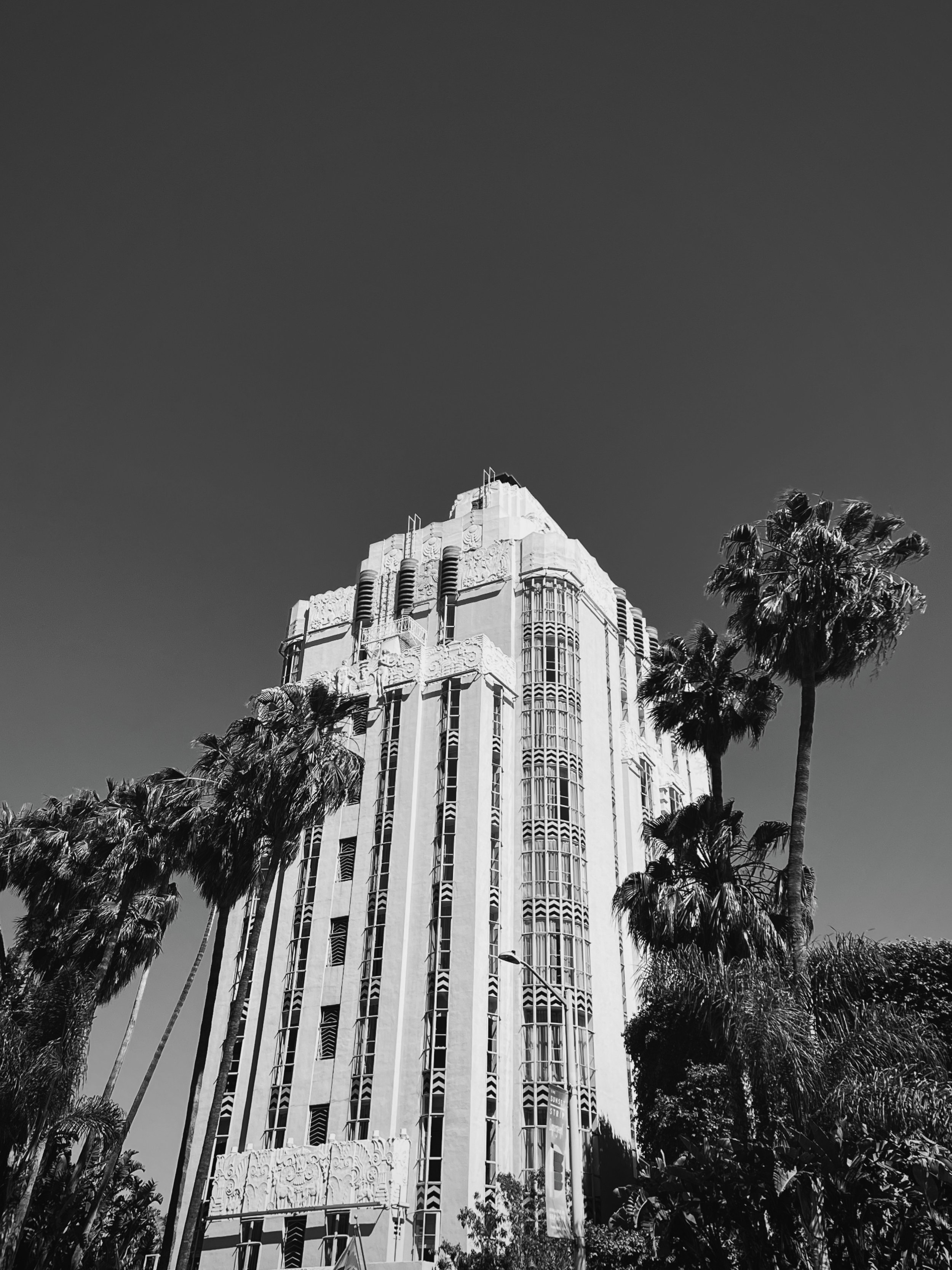 A tall art deco skyscraper surrounded by palm trees under a clear sky.