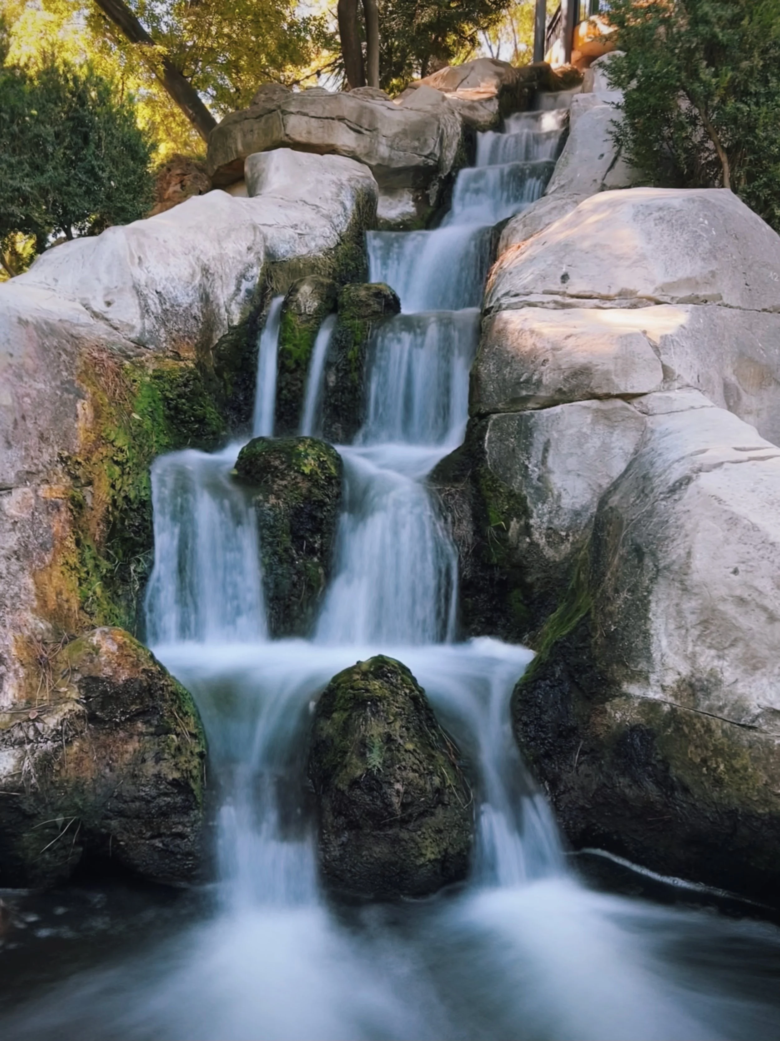 A multi-tiered waterfall cascading over rocks in a forested area during daytime.