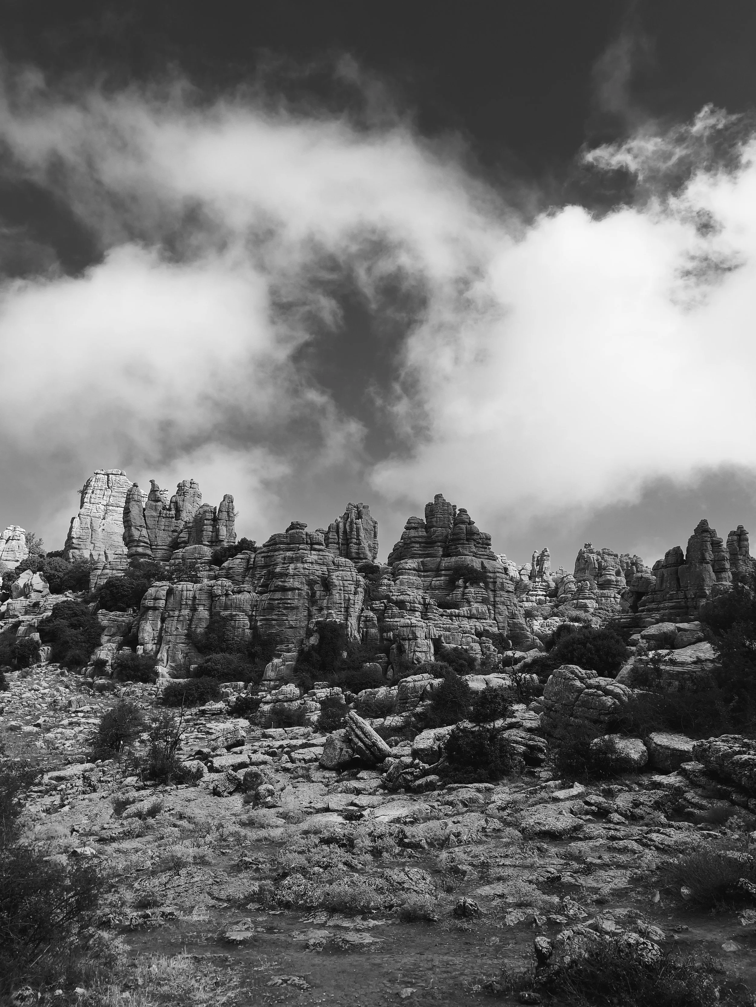 Black and white photograph of rocky mountain formations under a partly cloudy sky.