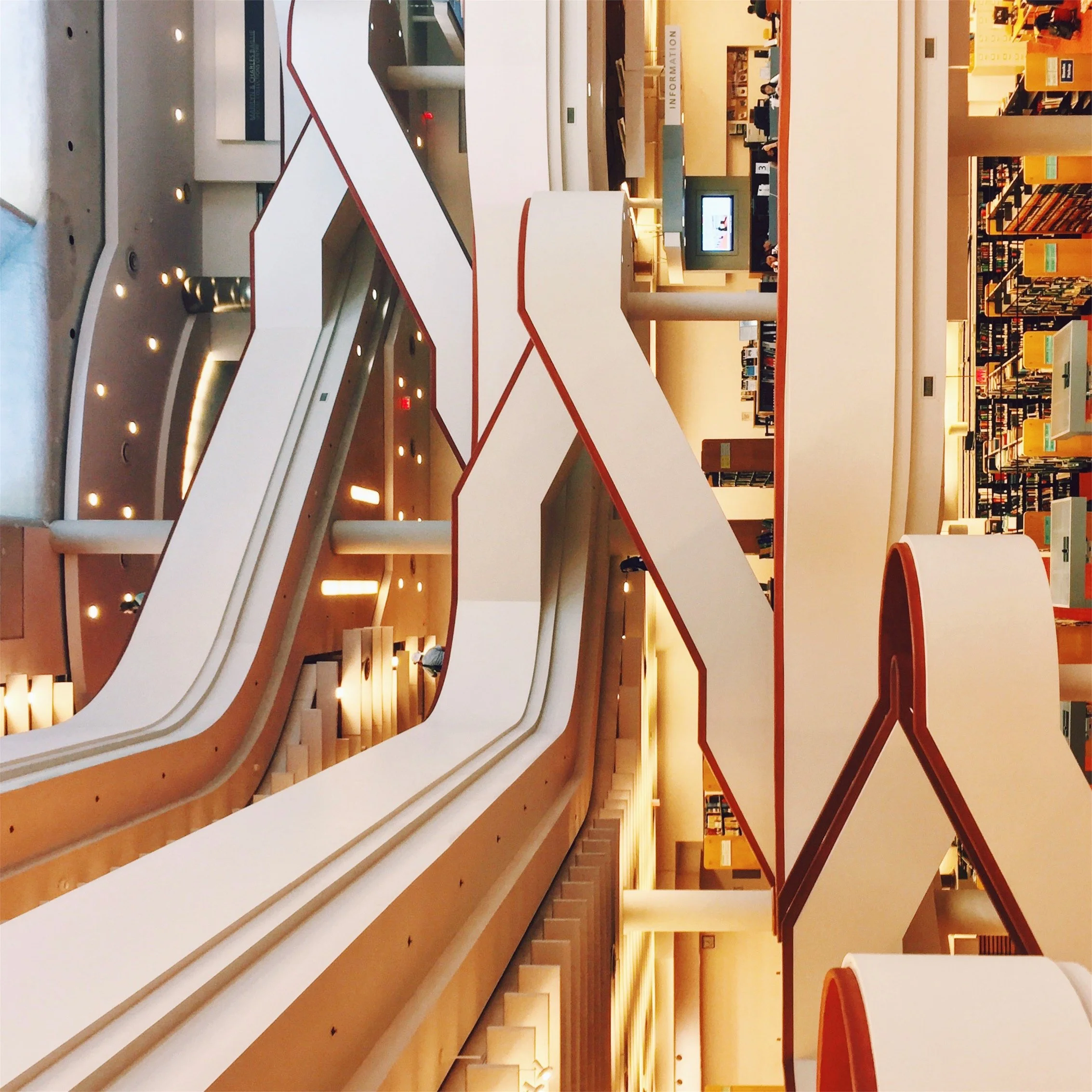 A multi-level modern library interior with white curved balconies with red edges and bookshelves filled with books in the background.