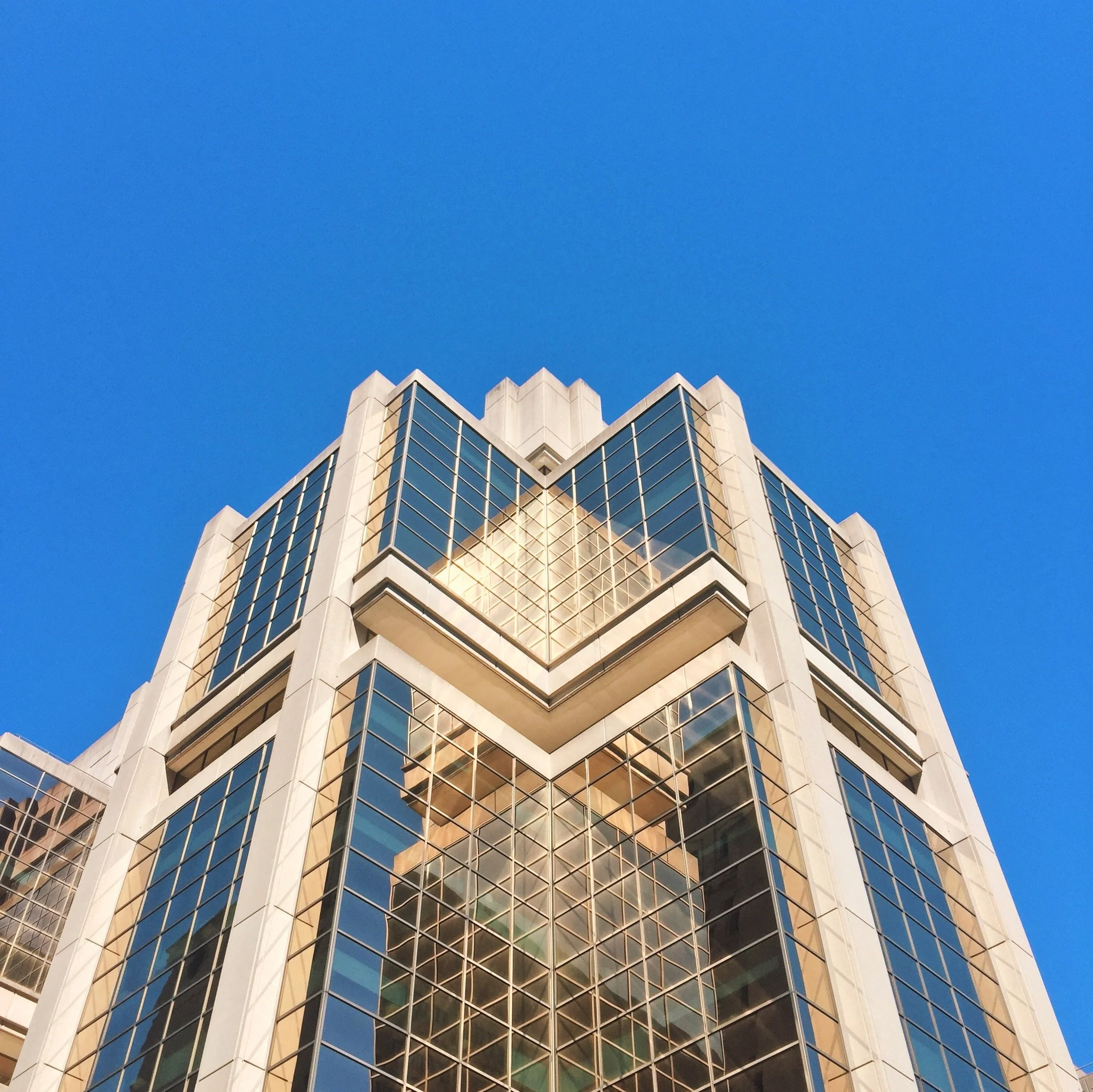 A modern high-rise building with glass windows reflecting the sky, taken from a low angle against a clear blue sky.