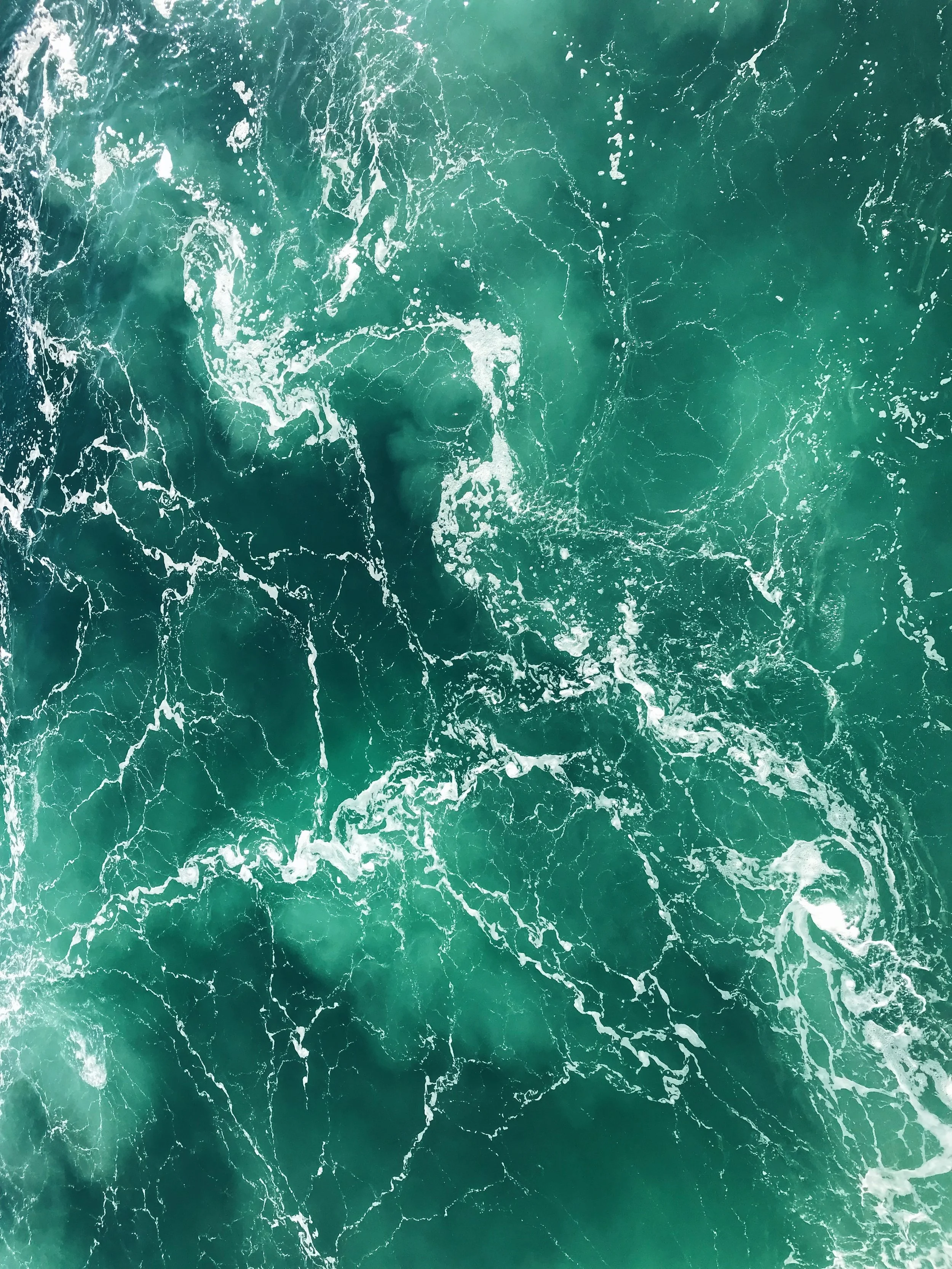 An aerial view of a whirlpool or vortex in the ocean with swirling water and white foam.