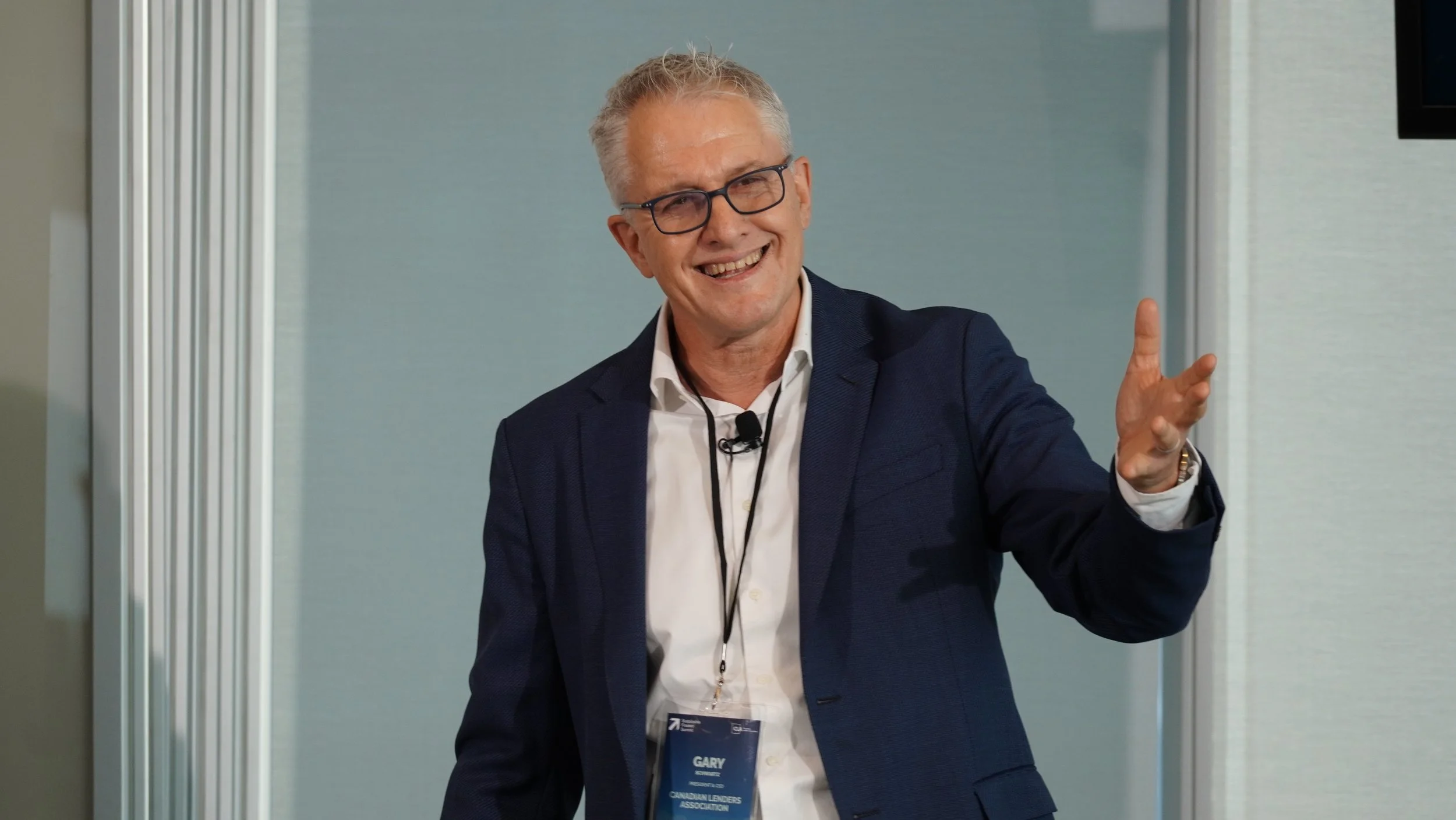 A man with gray hair and glasses gesturing with his hand during a presentation.