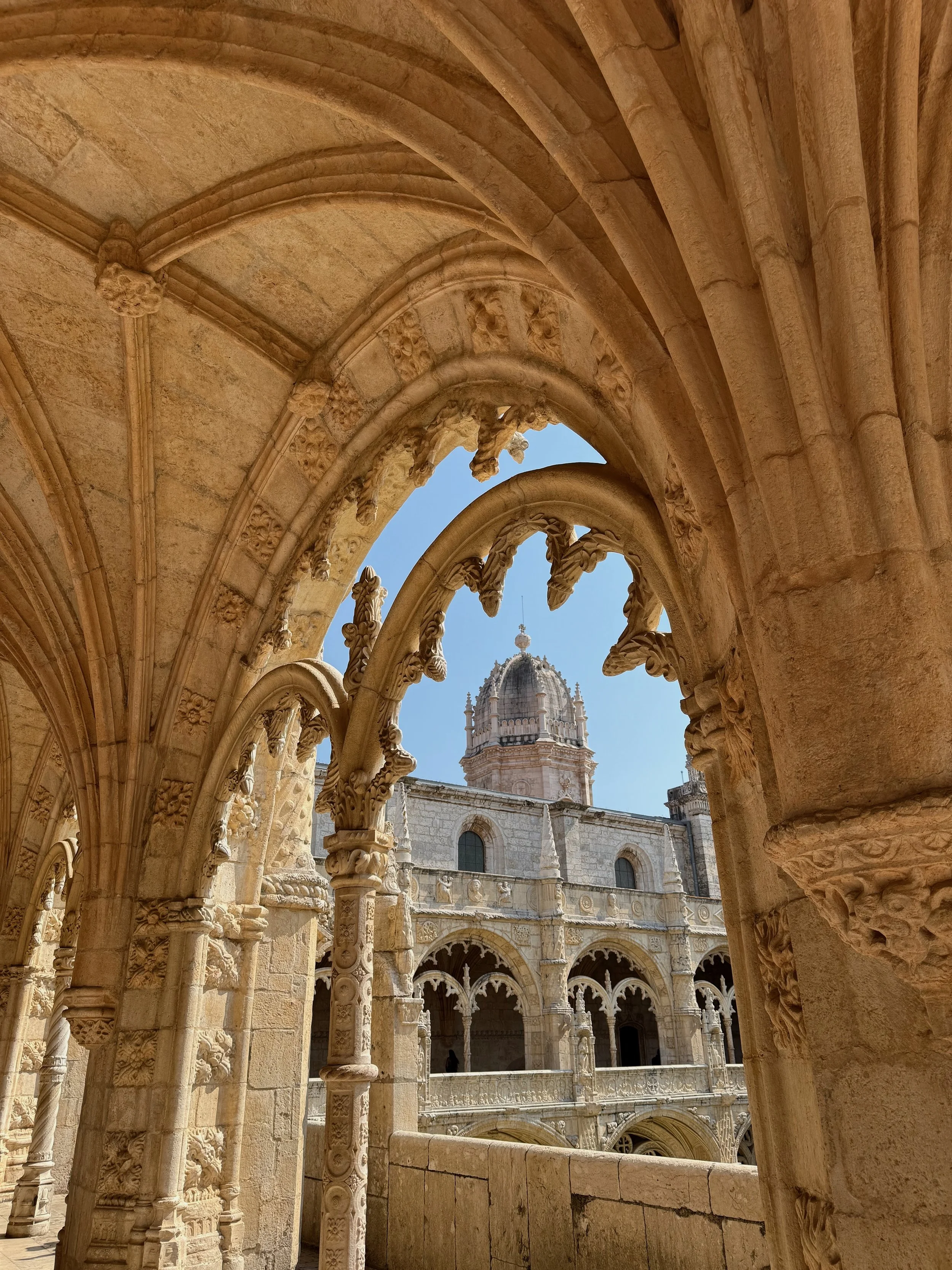View of an ornate stone cathedral through arched windows with intricate carvings, showing a clear blue sky.