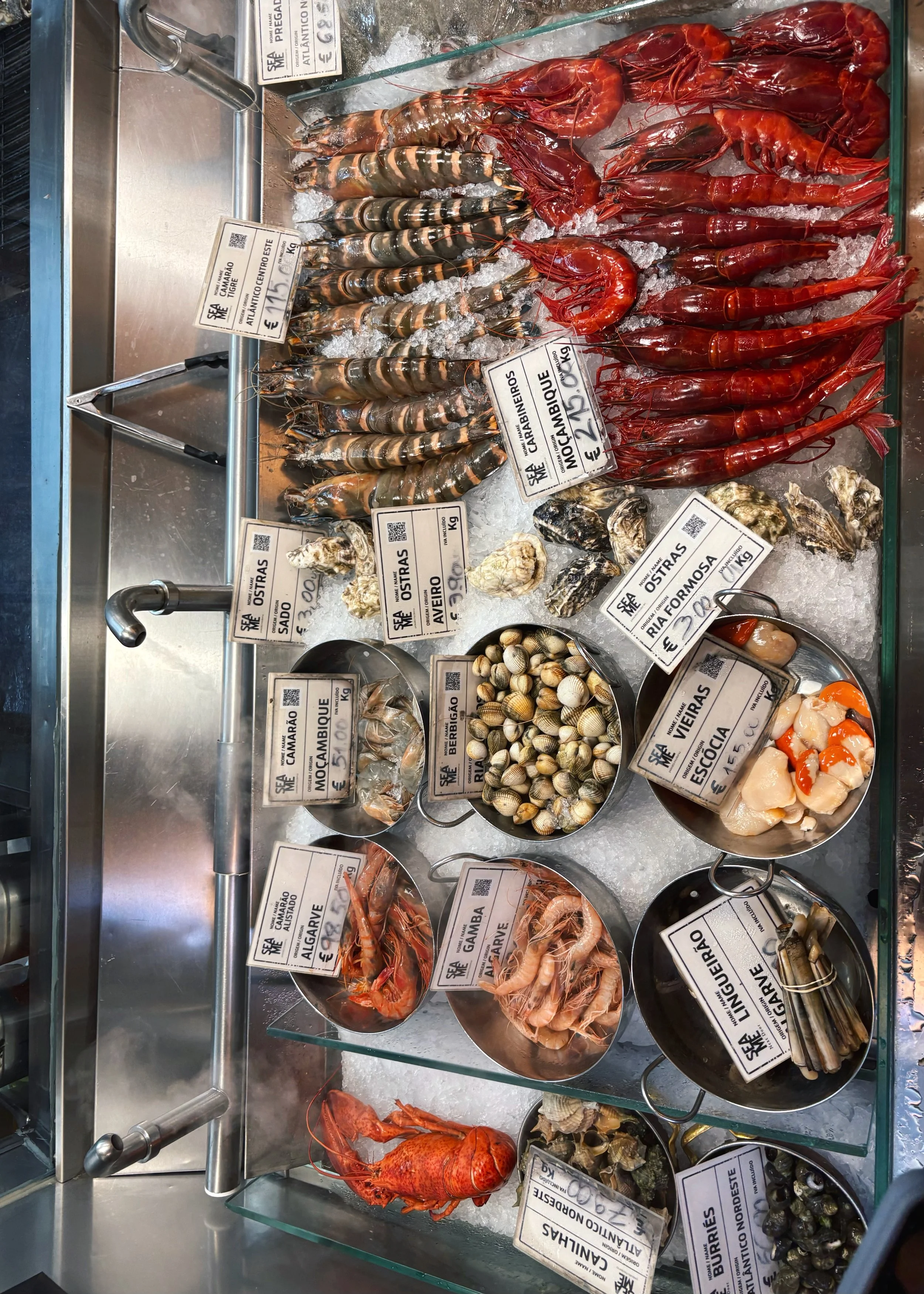Display of fresh seafood on ice, including shrimps, crabs, clams, oysters, and scallops at a seafood market.
