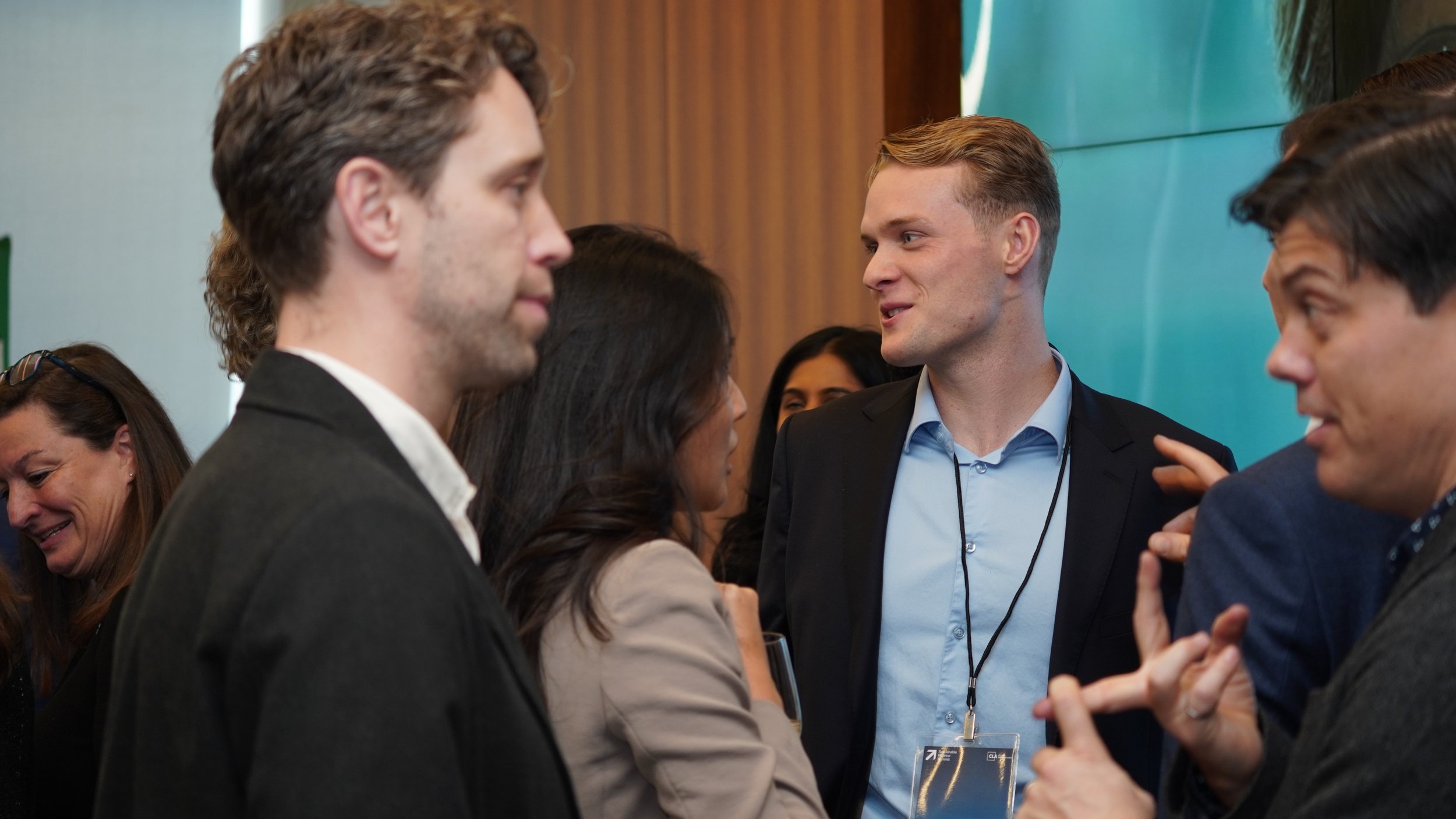 People engaged in conversation at a professional networking event or conference, with men and women interacting in a lively setting.