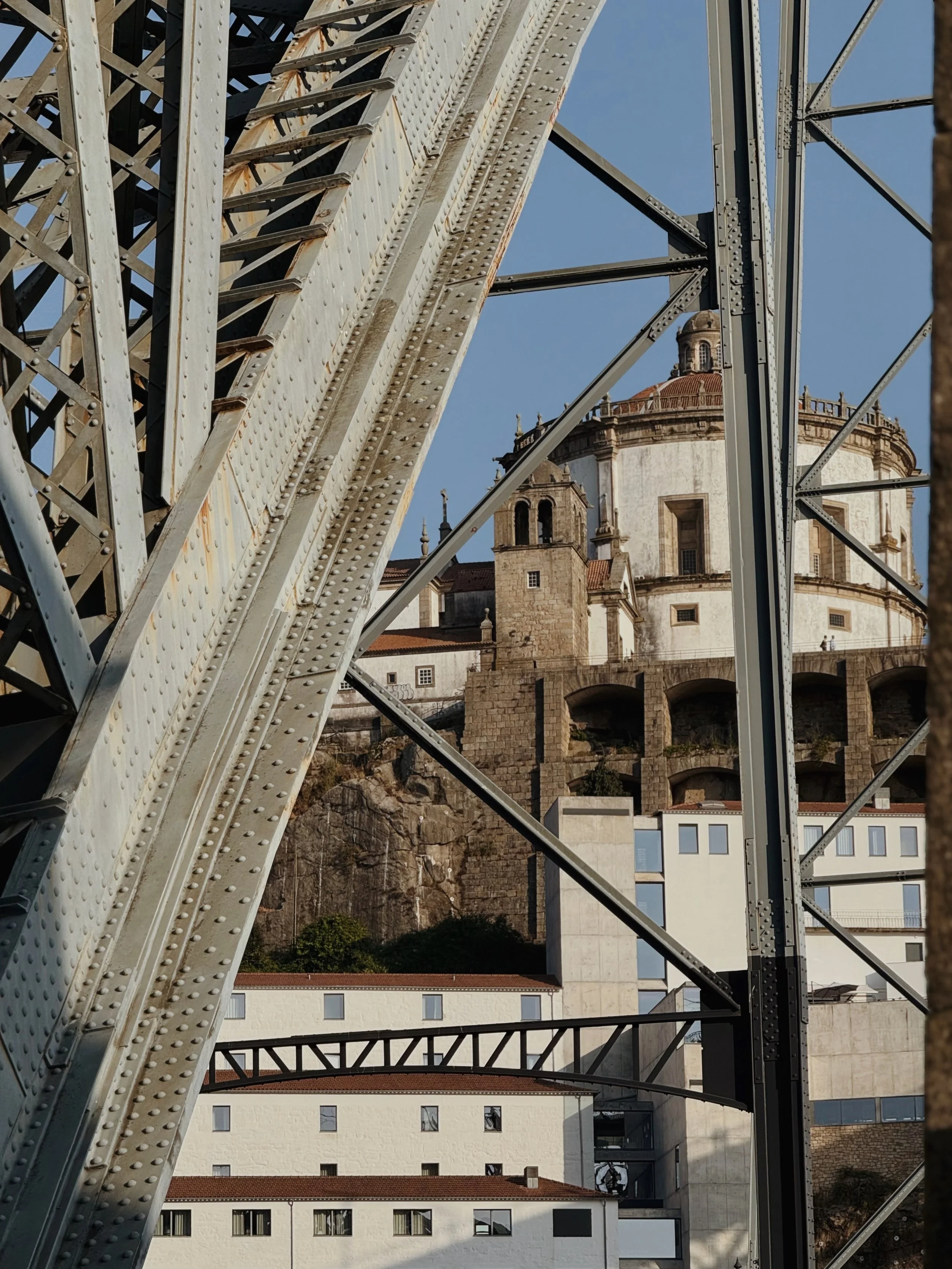 View of a historic church and buildings on a hillside framed by the structure of a bridge.