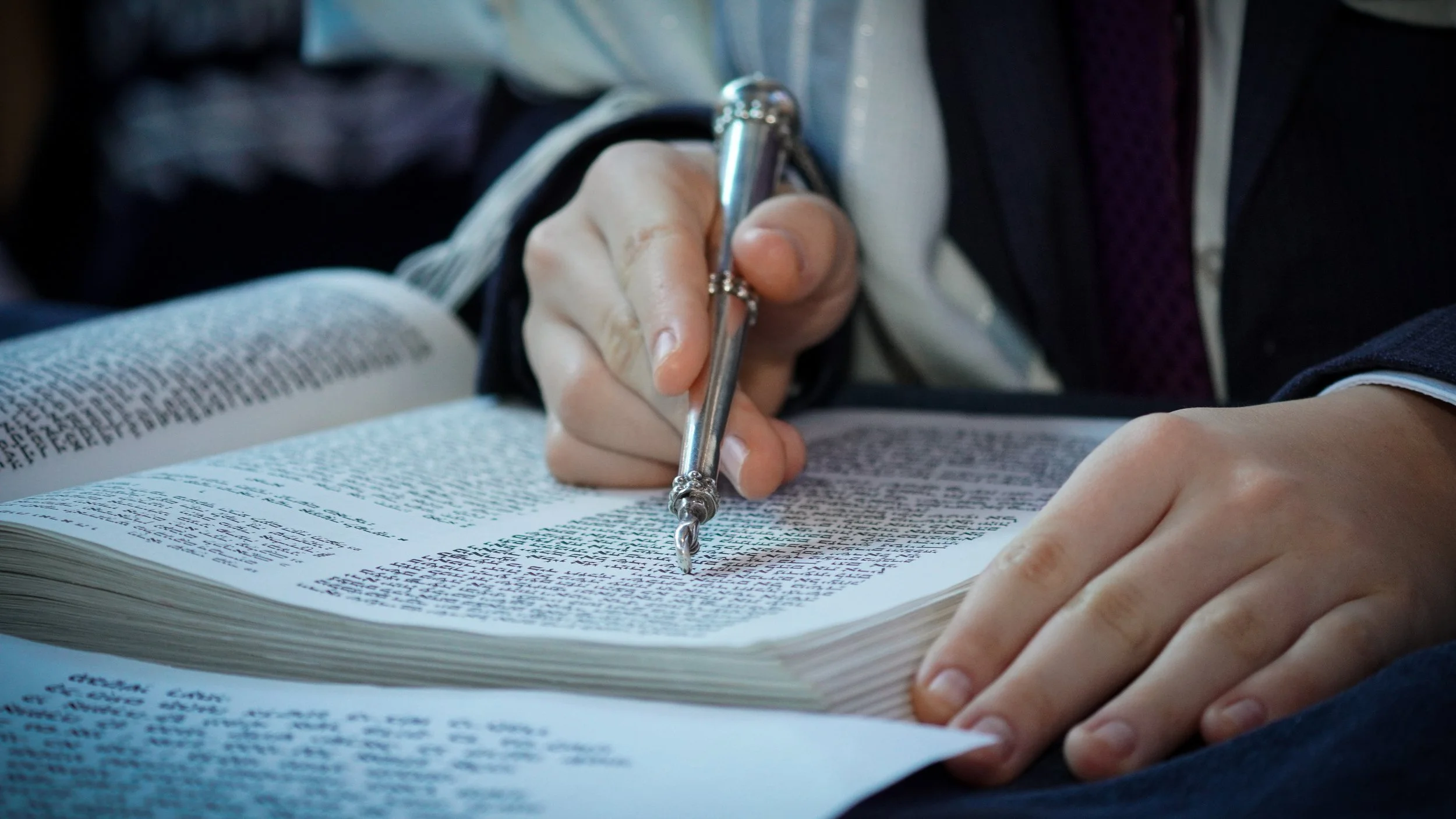 Person in a suit using a vintage style metal fountain pen to write in a large printed book.