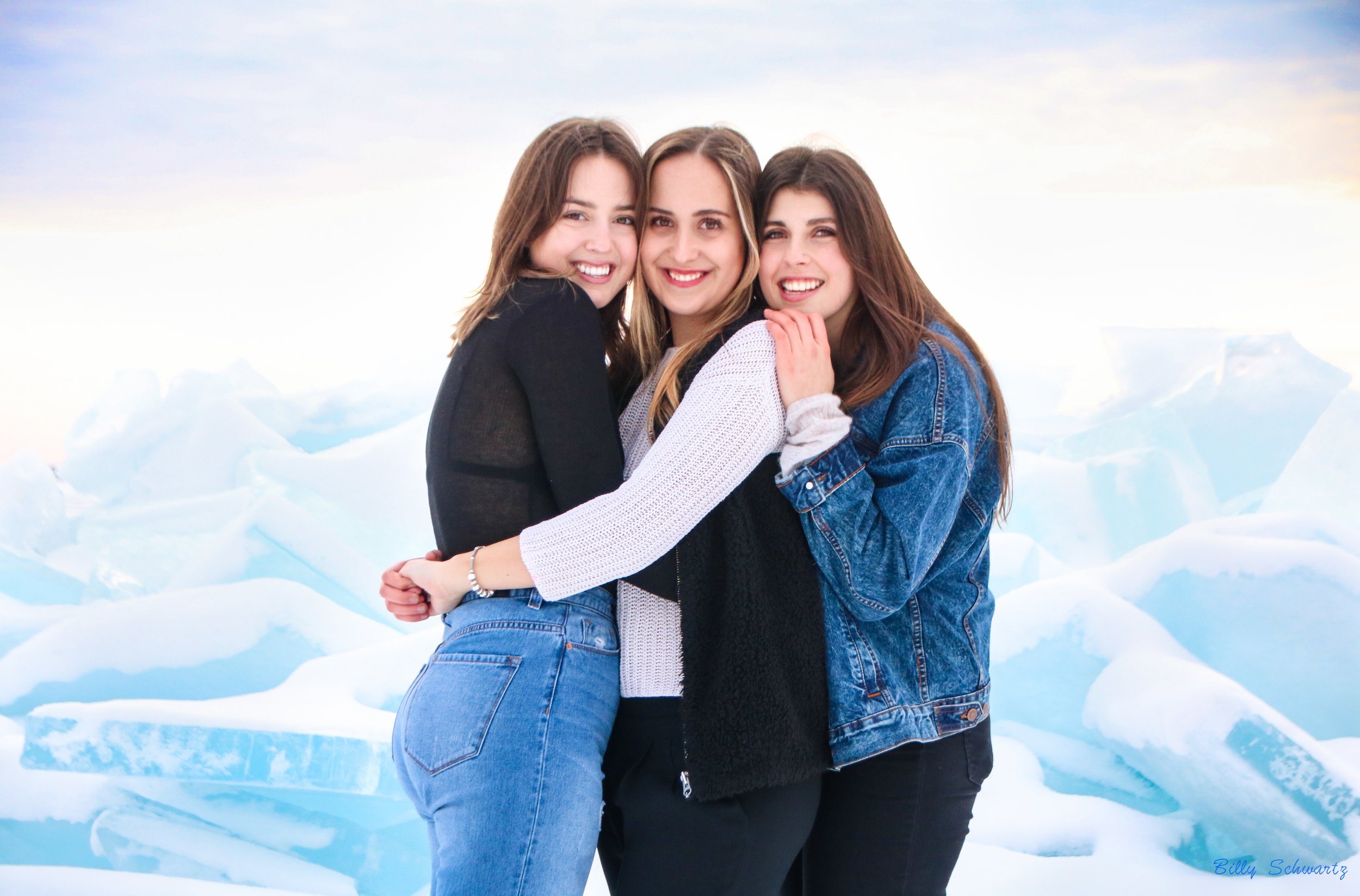 Three women smiling and hugging each other outdoors with ice and snow in the background.