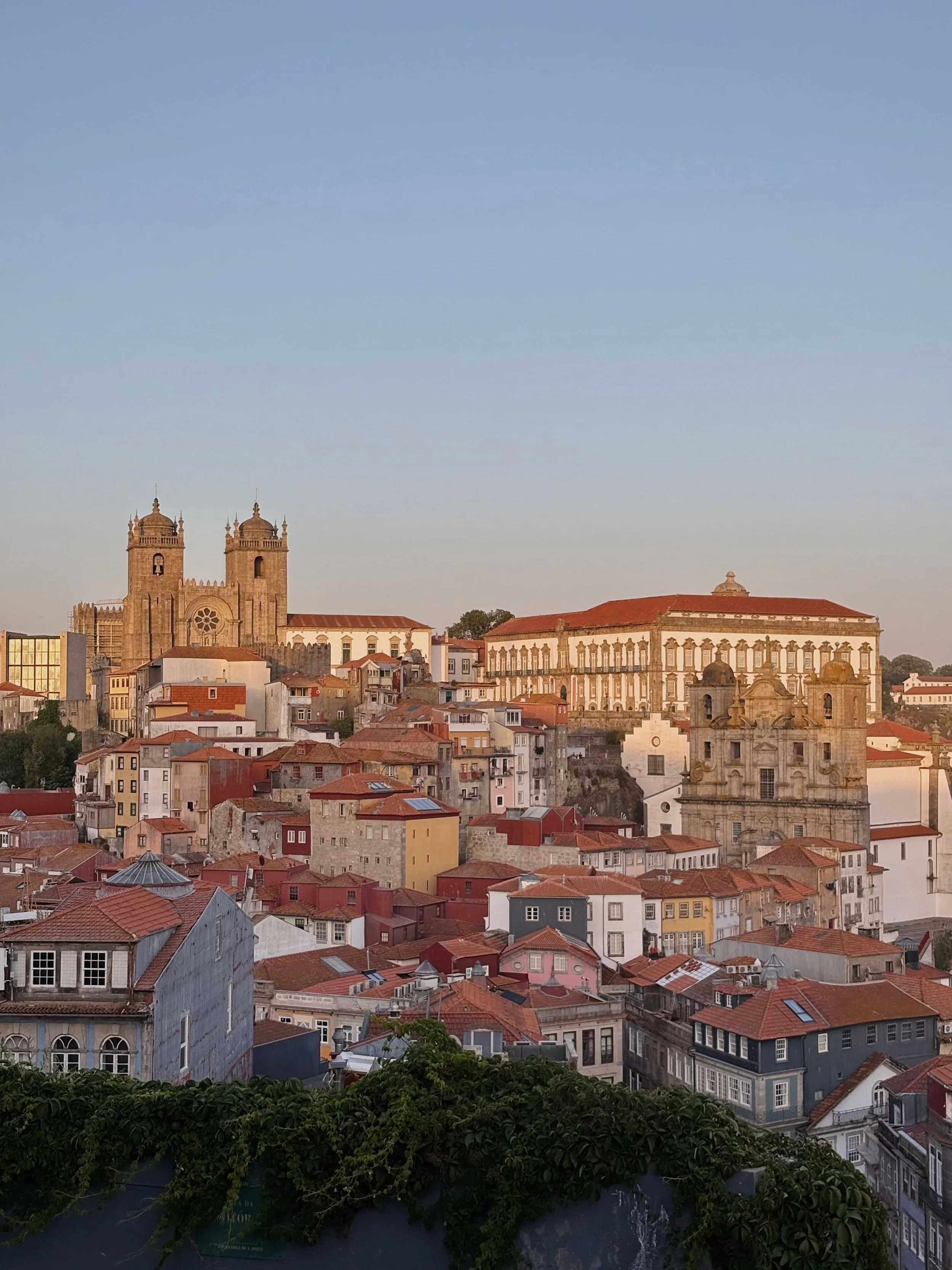 A panoramic view of a historic European city with colorful buildings, red-tiled roofs, and prominent cathedral and church structures on a clear day.