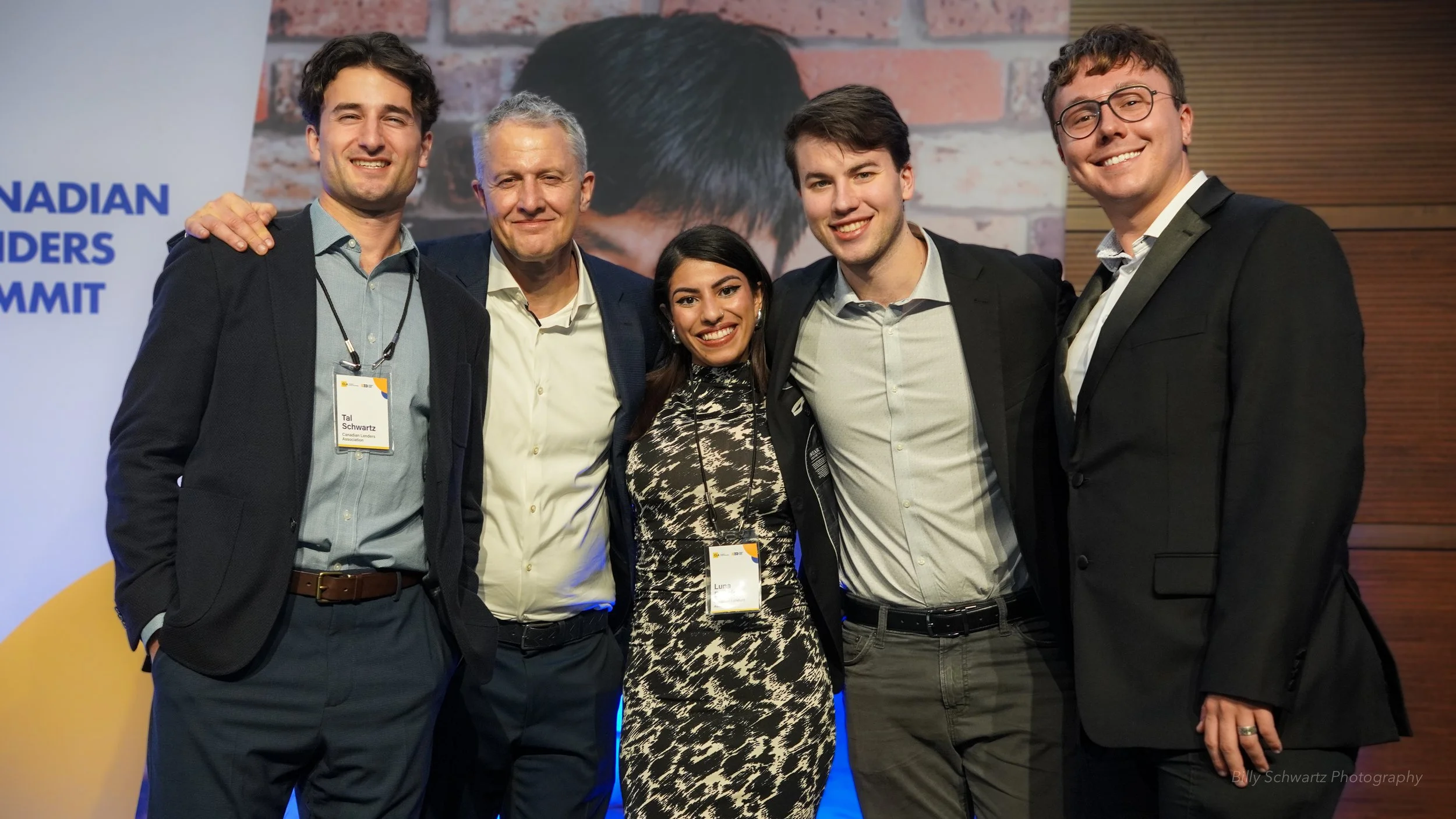 Five people standing together at a formal event, smiling at the camera, wearing business attire, with a backdrop indicating a Canadian Leaders Summit.