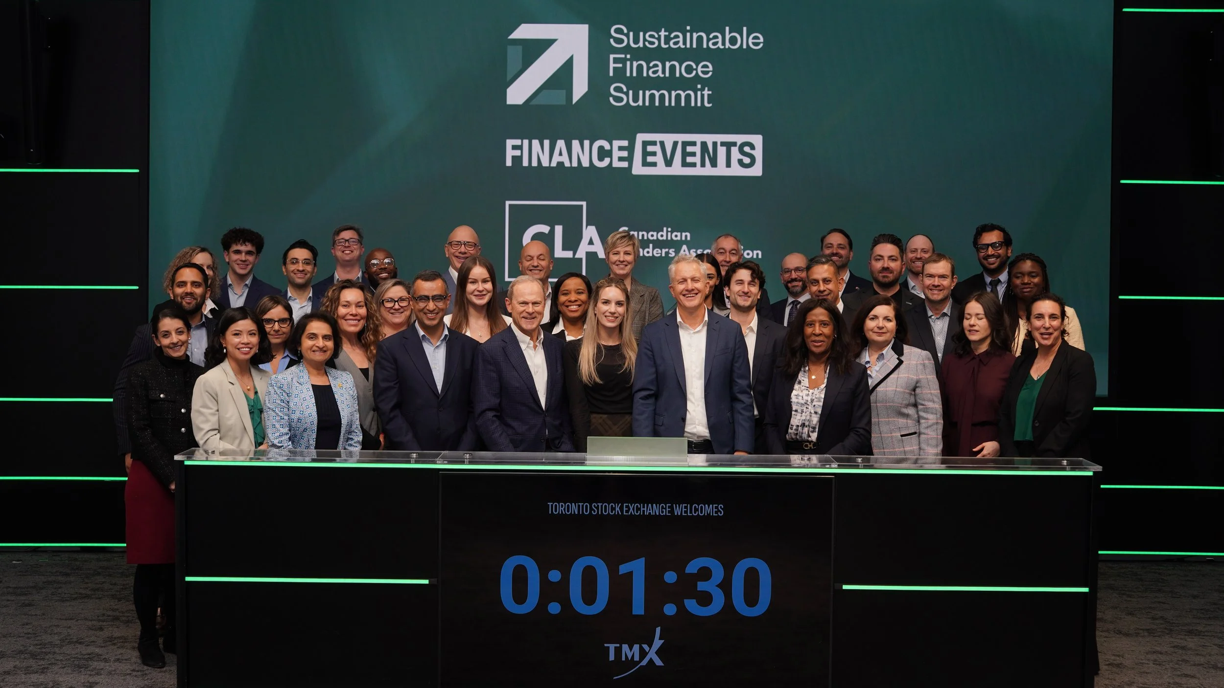 A group of professionals on stage at the Sustainable Finance Summit, standing behind a digital countdown timer showing 1 minute and 30 seconds, with a large screen behind them displaying event information, including 'Finance Events' and 'Canadian Lea