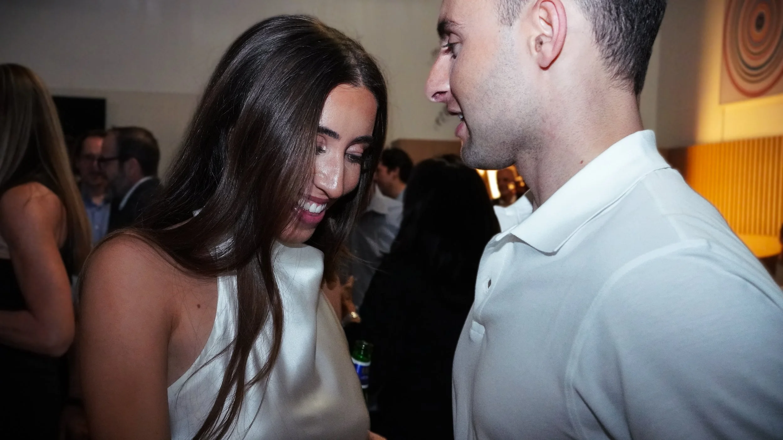 A woman and a man are smiling and looking at each other at a social event.