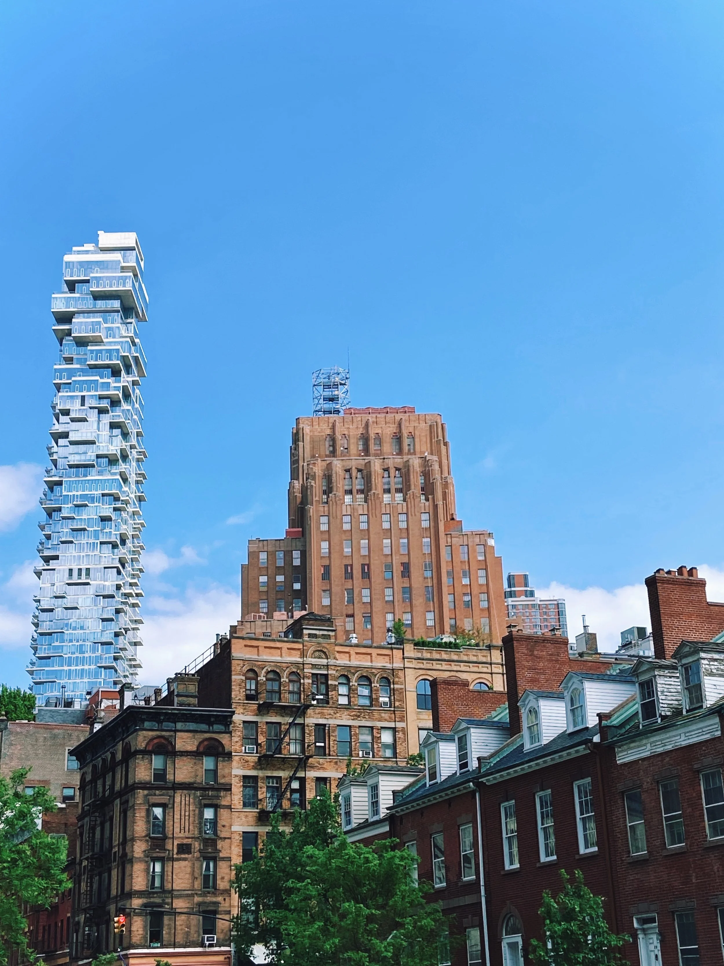 City skyline with modern and historic buildings under a clear blue sky, with greenery in the foreground.