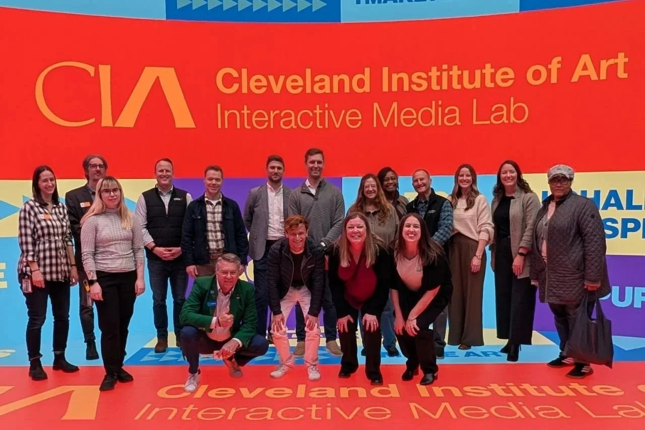 Group of people posing for a photo in front of a large colorful backdrop with text 'Cleveland Institute of Art Interactive Media Lab'.