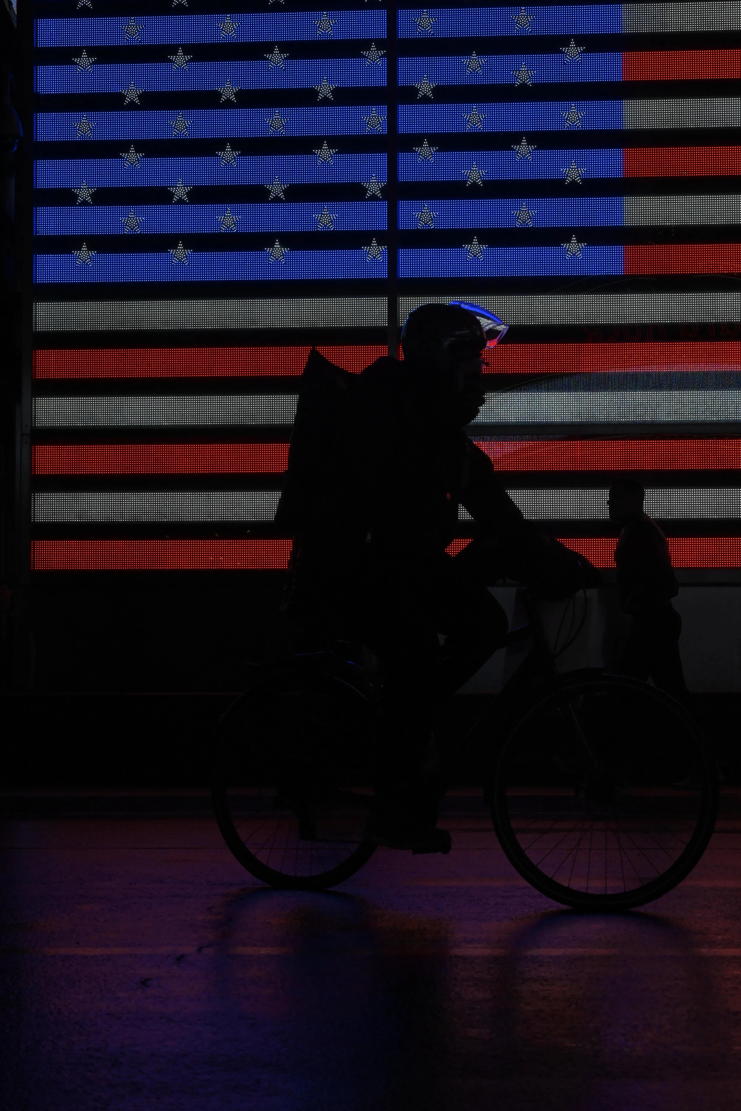  Delivery driver silhouette in front of iconic American Flag light mural in Times Square, Manhattan. 