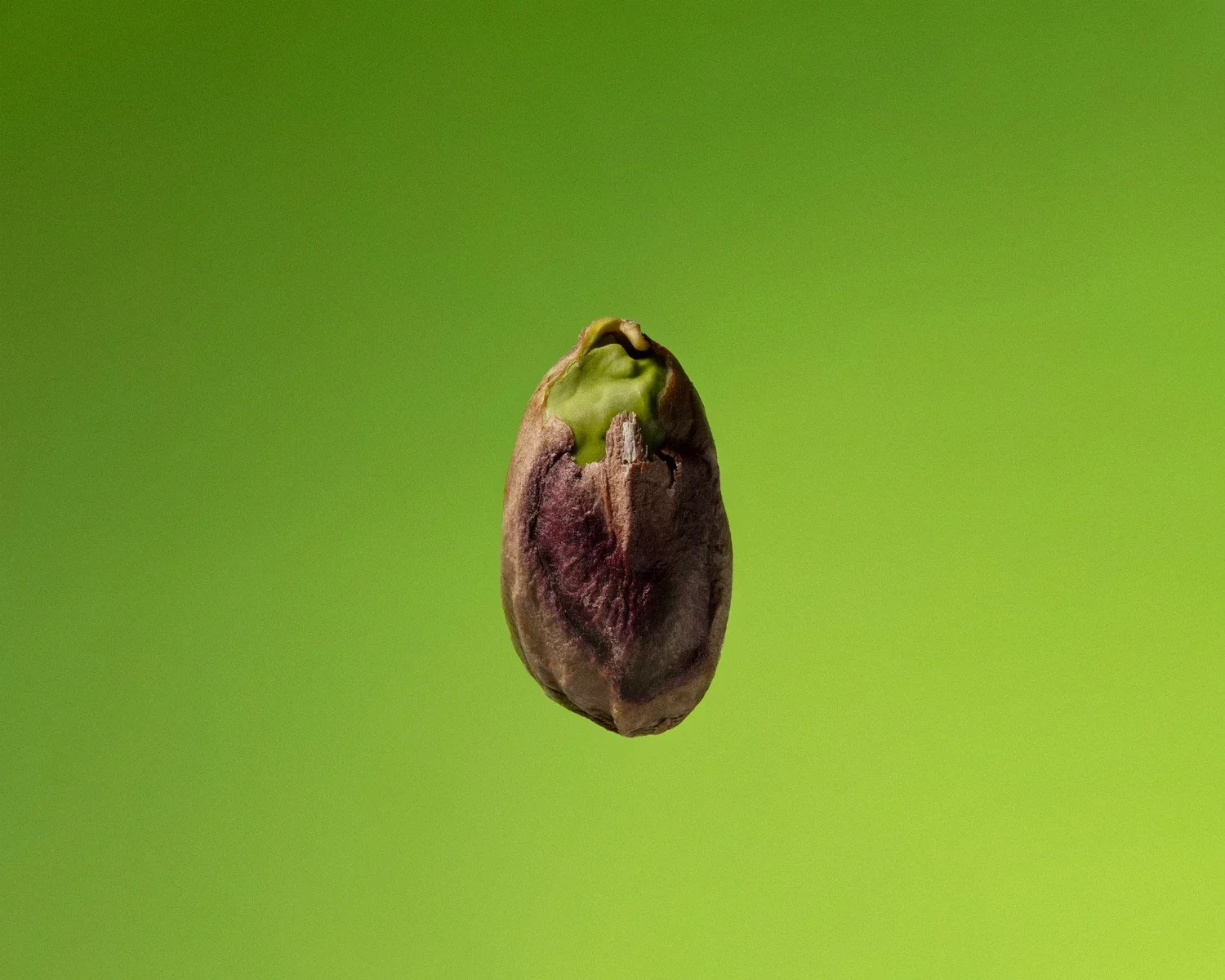 A close-up of a pistachio nut with a cracked shell, revealing the green kernel inside, against a blurred green background.