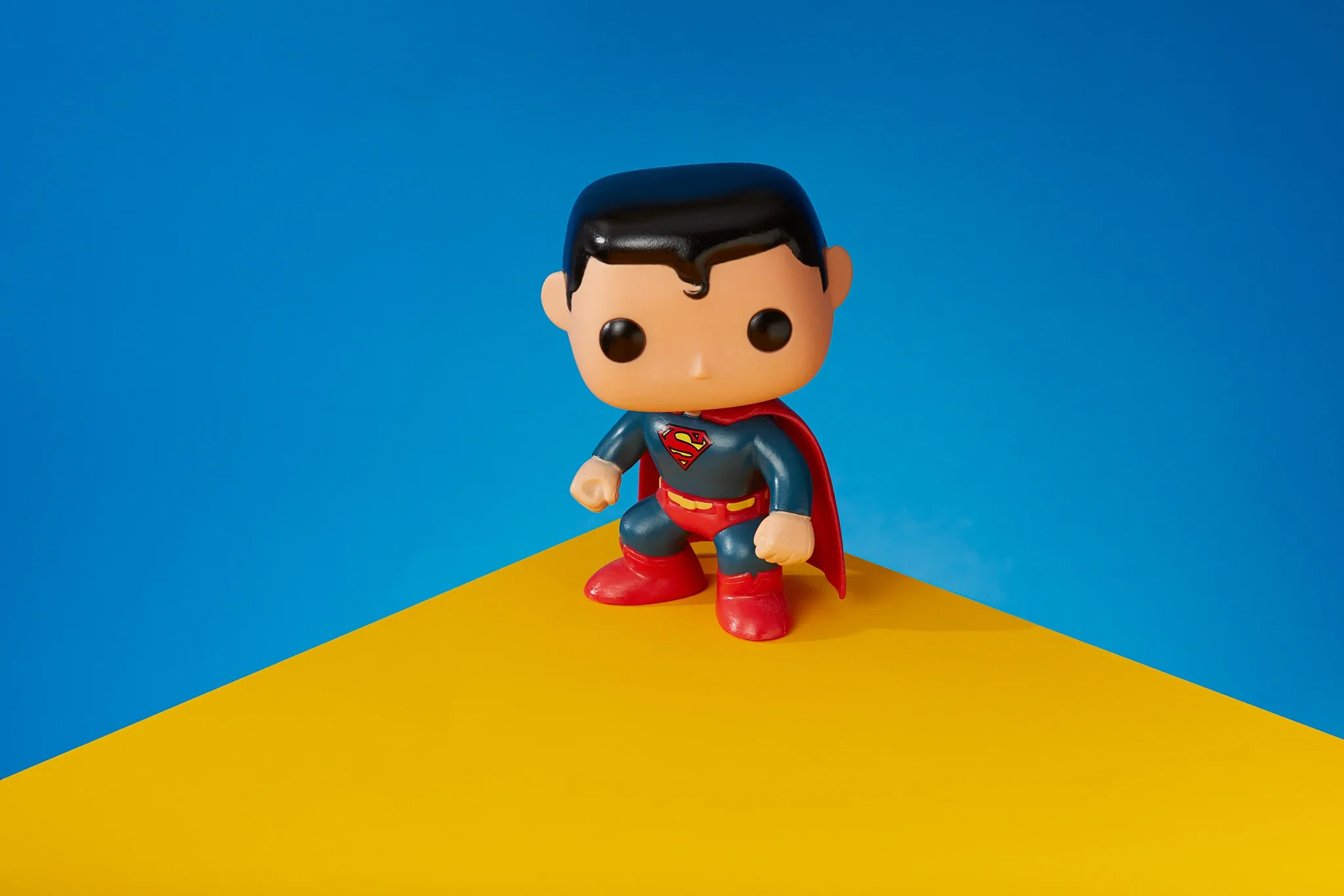 A stylized Superman figure standing on a yellow and blue surface with a blue background.