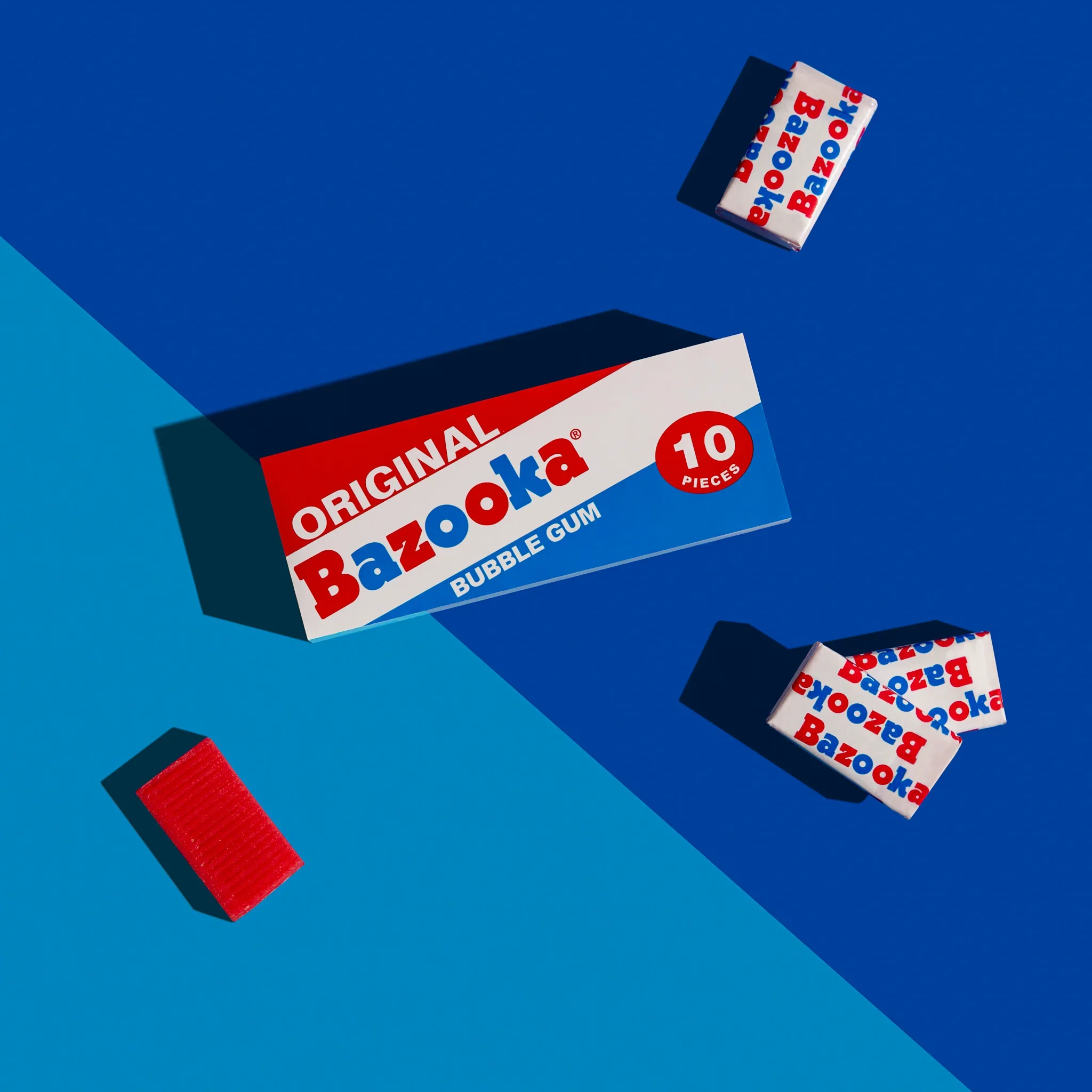 Box of Bazooka bubble gum on a blue background with other gum packets.