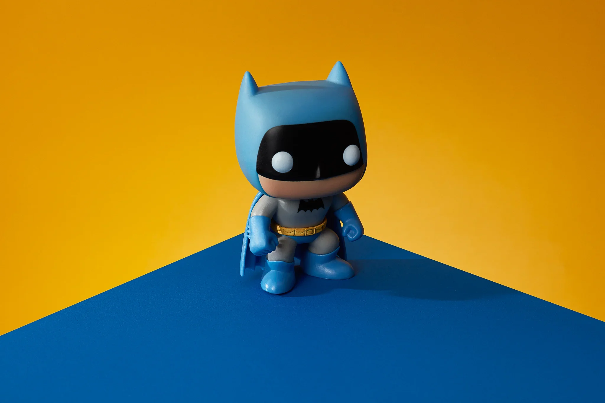 A small Batman-themed Funko Pop toy figure standing on a blue and yellow background.