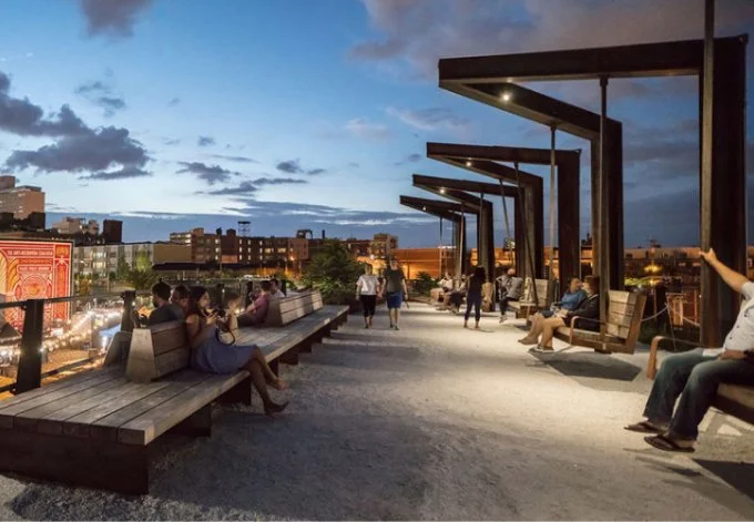 Individuals are seated on benches atop a high line, surrounded by greenery and city views, creating a tranquil urban retreat.