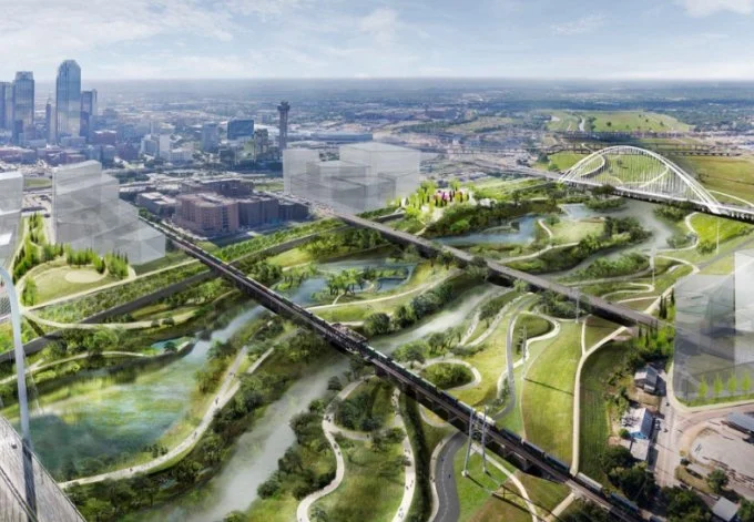 Aerial view of a cityscape with green parks, meandering waterways, bridges, and modern buildings under a blue sky.