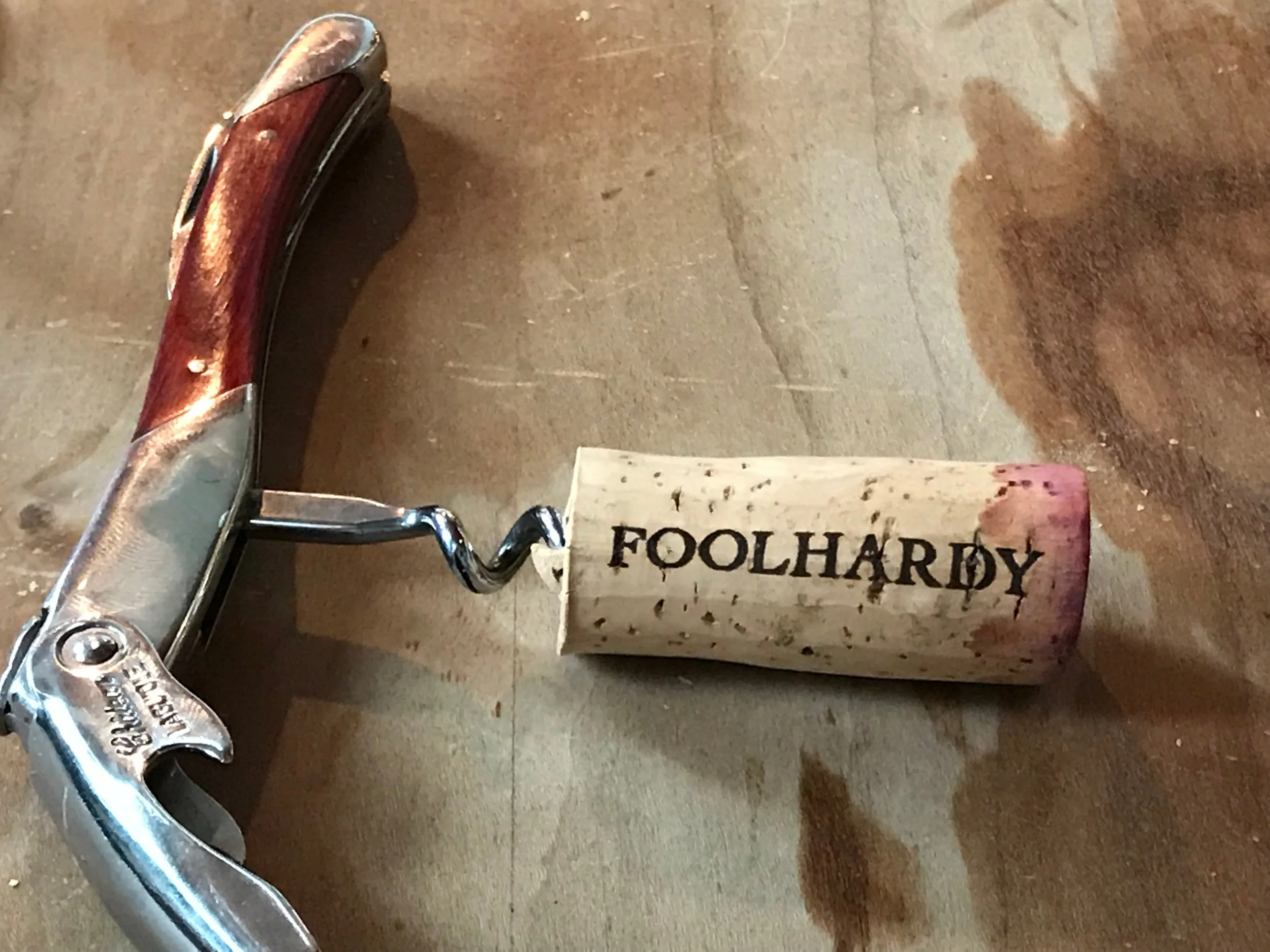 A Foolhardy cork impaled on a wine key laying on a wine-stained table