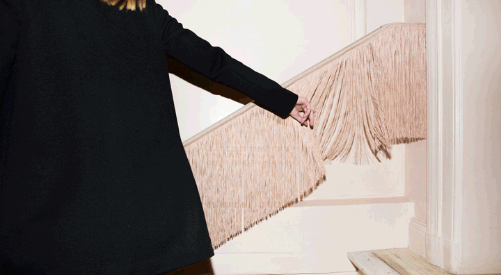 Girl passing her hand along stairwell railing fringe as she walks down the stairs at Moda Operandi retail store in New York City