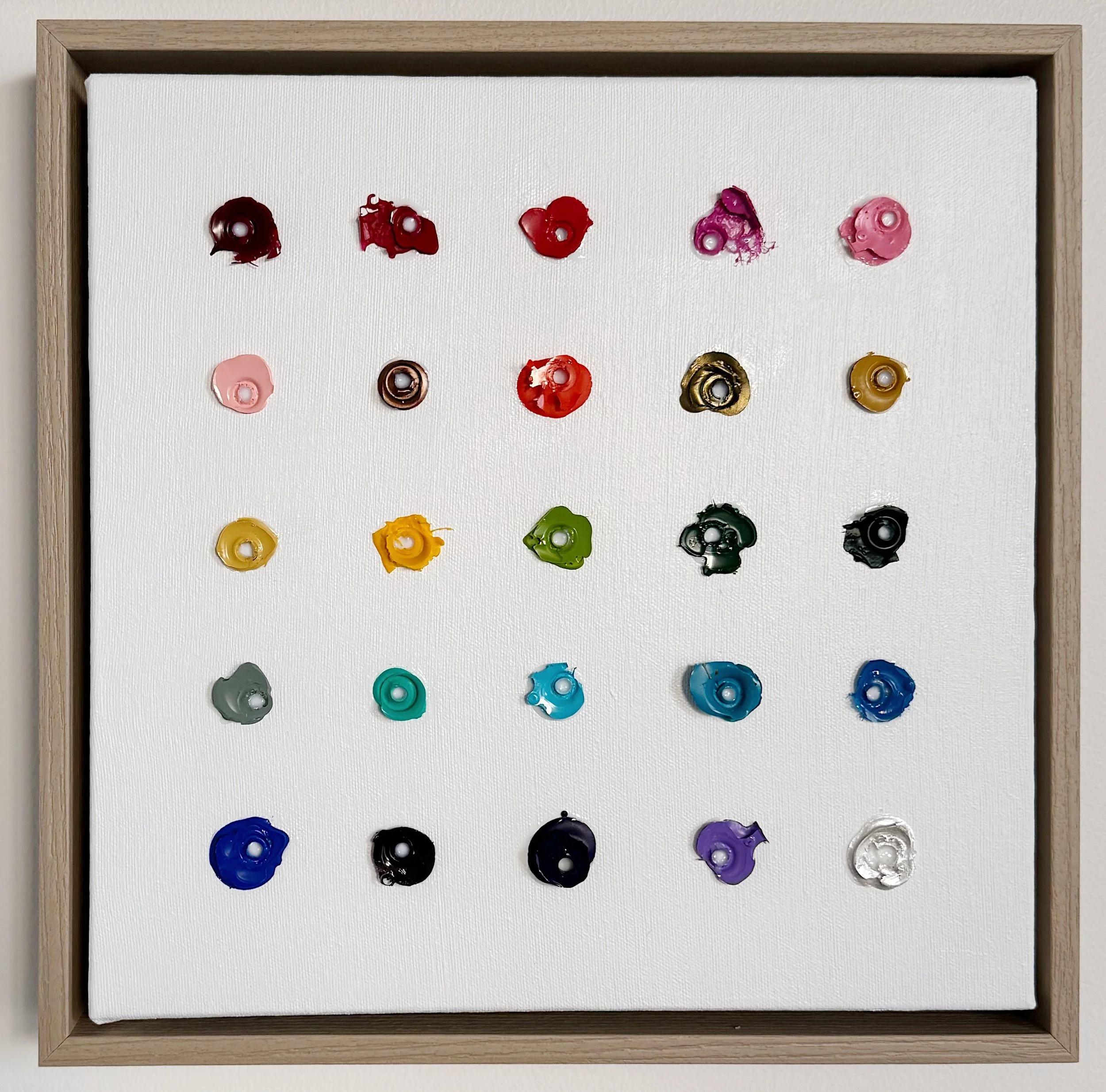 Square original painting on canvas displaying five rows and five columns of small organic circles of dried acrylic paint, rainbow colored in nature, mounted on a white canvas within a light wood frame.